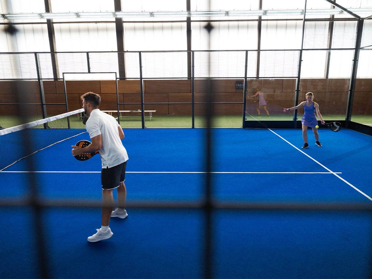 Två personer spelar padel på en blå bana, mannen håller ett racket.