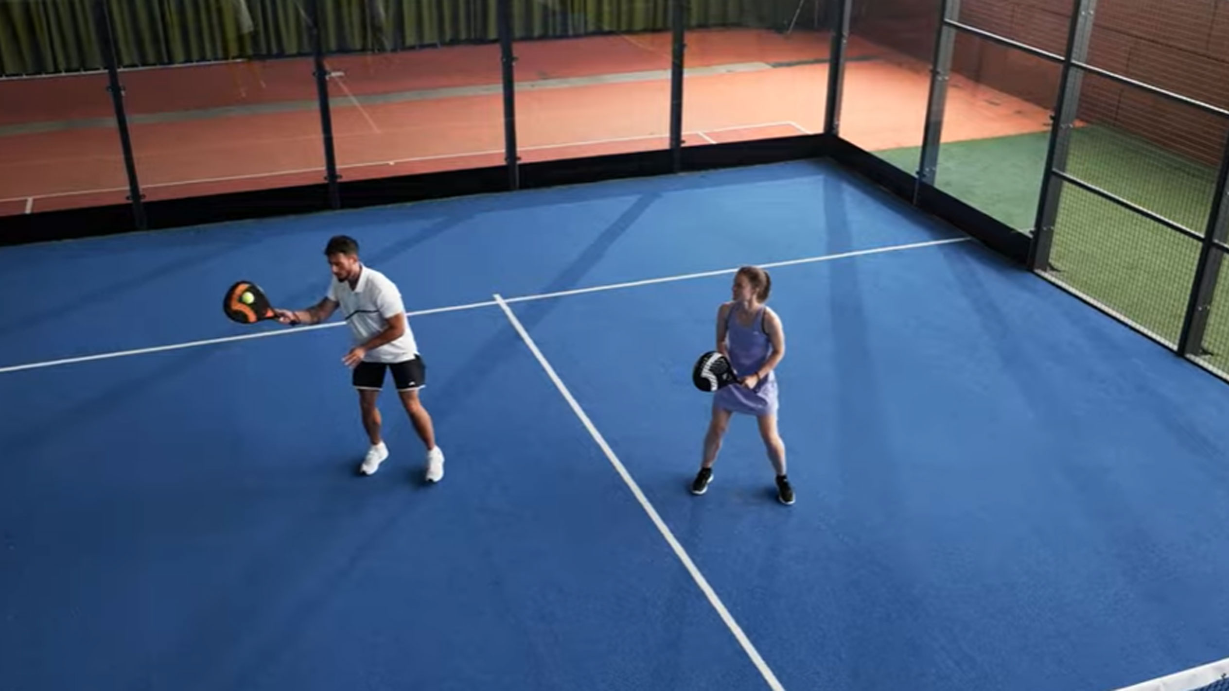 Man och kvinna spelar padel på blå bana med racketar och boll