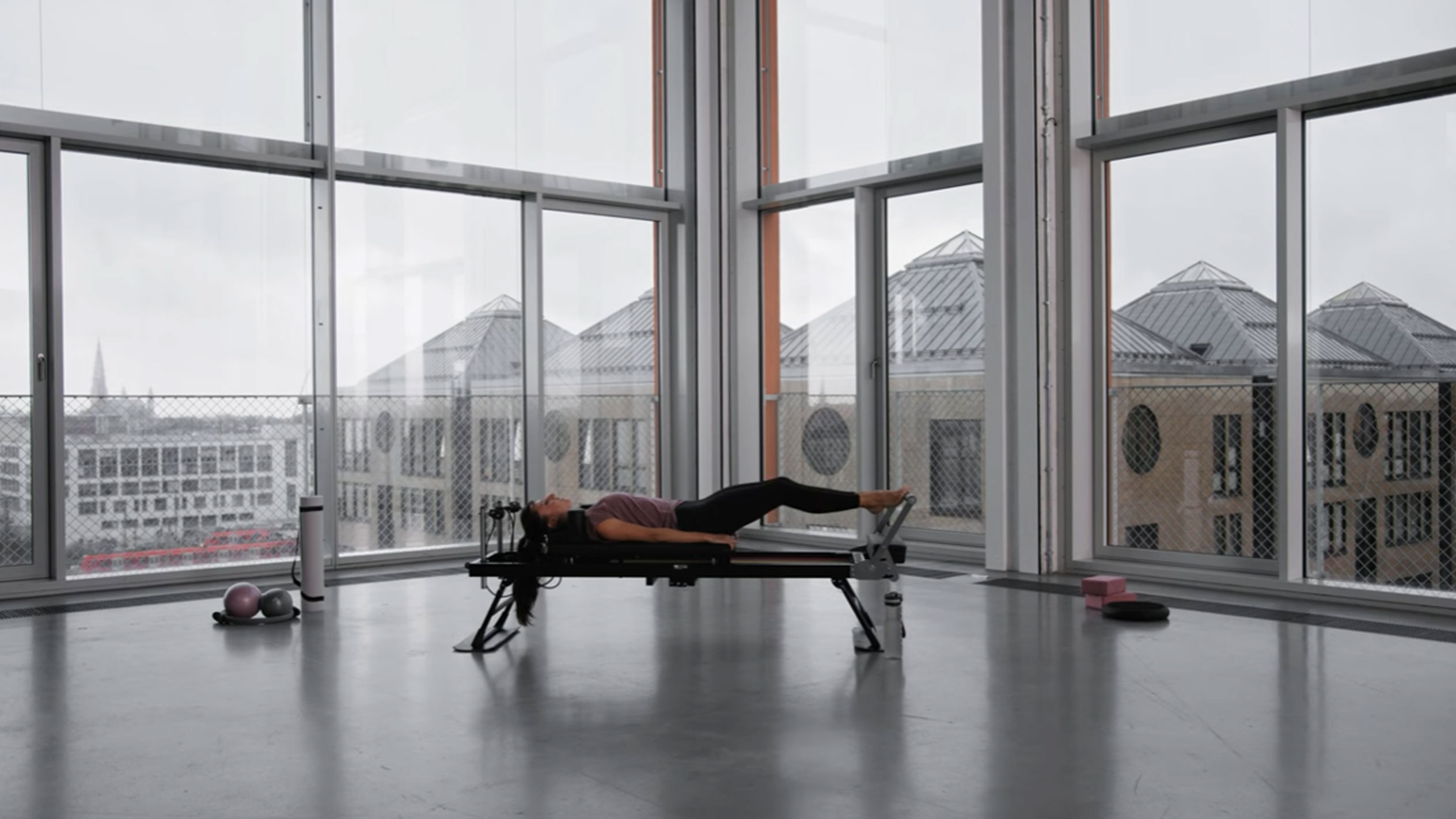Kvinna som tränar Pilates i modern studio med utsikt över staden.