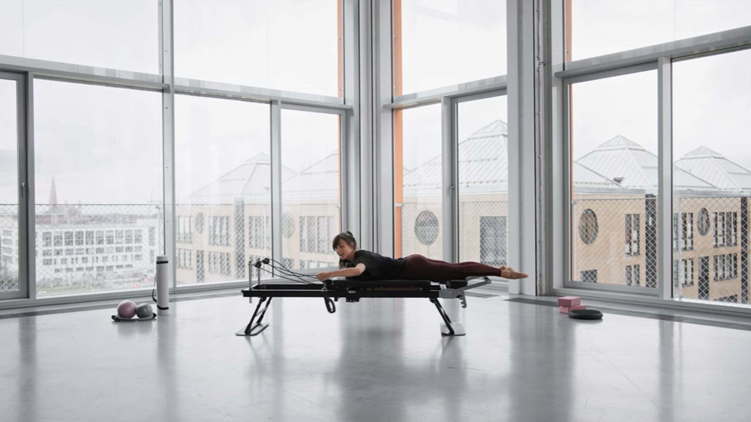 Kvinna som tränar Pilates på en reformer, med utsikt över staden.