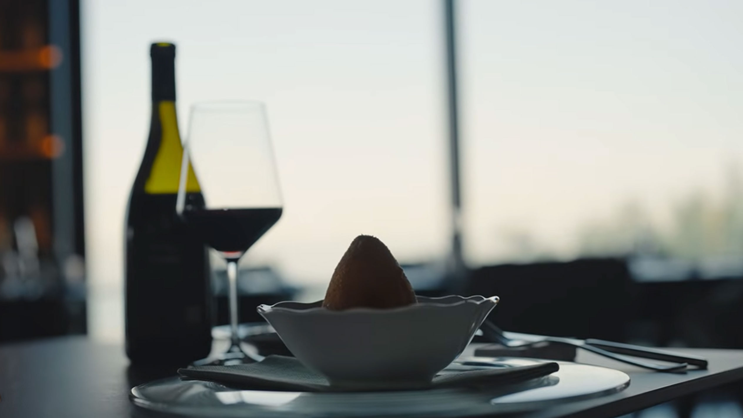 En flaska rött vin och ett glas bredvid en arancino i en skål på ett bord.