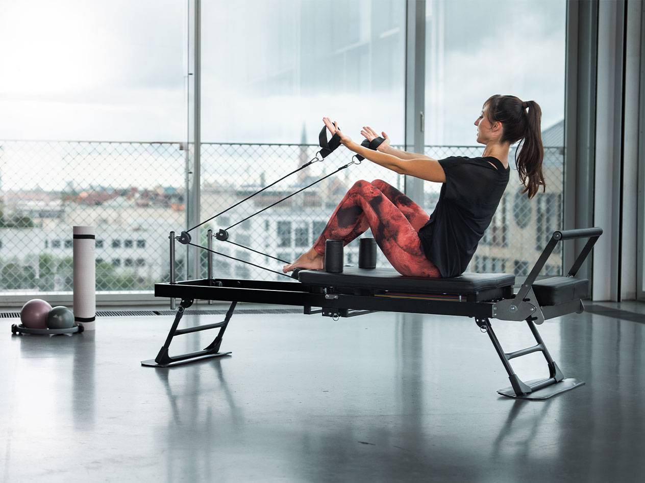 Kvinna tränar pilates på en reformer med utsikt över staden.