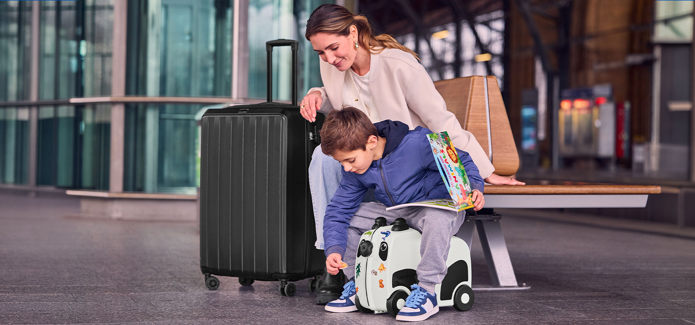 Mor och barn med bagage på flygplatsen, barnet leker med en åkresväska.