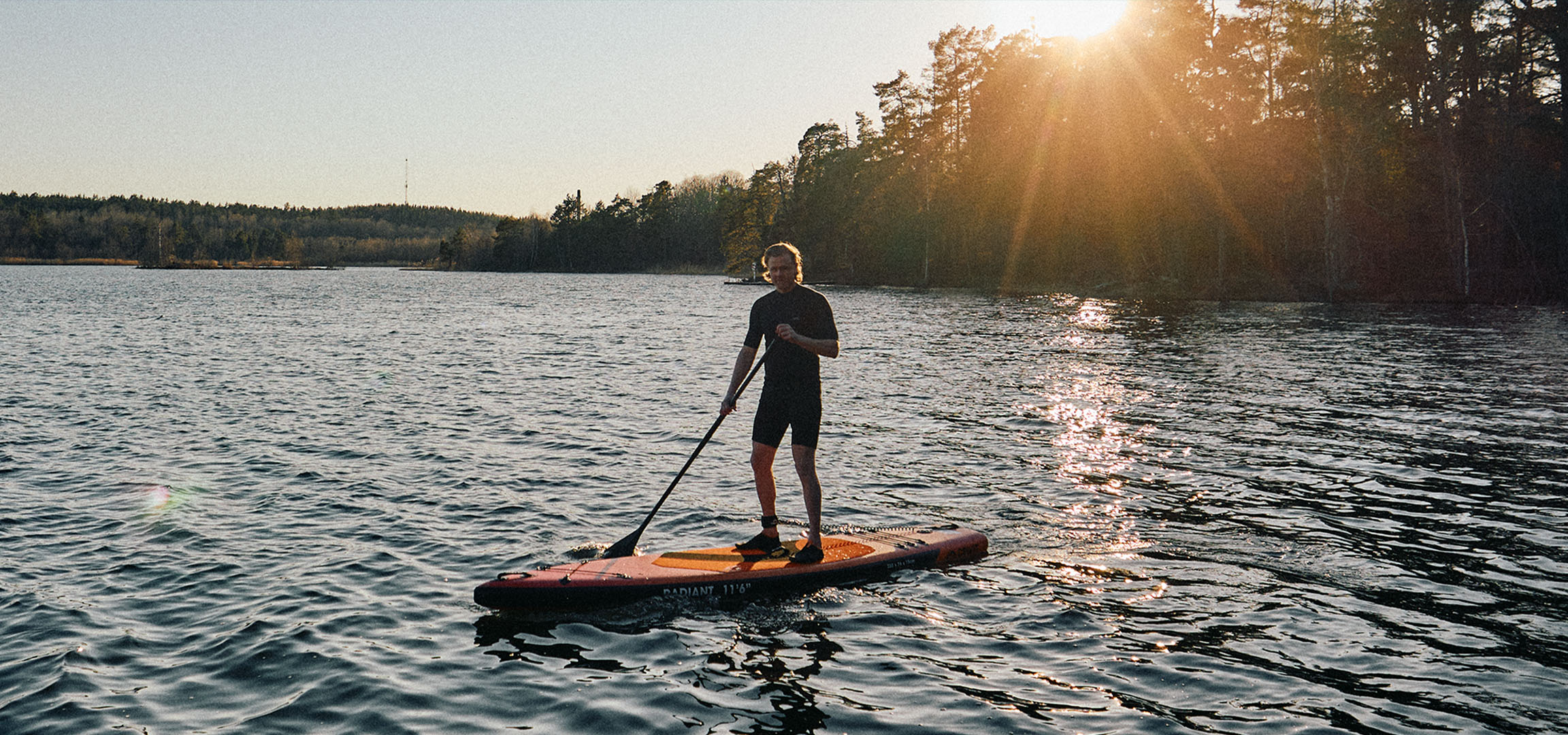 Man på en stand up paddleboard på en sjö vid solnedgången.
