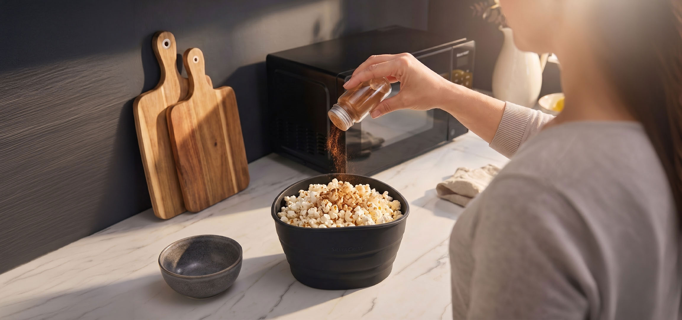aiLabeling.aiLabelForImageAltText: Popcorn i en svart skål kryddade med kryddor, bredvid skärbrädor i trä.