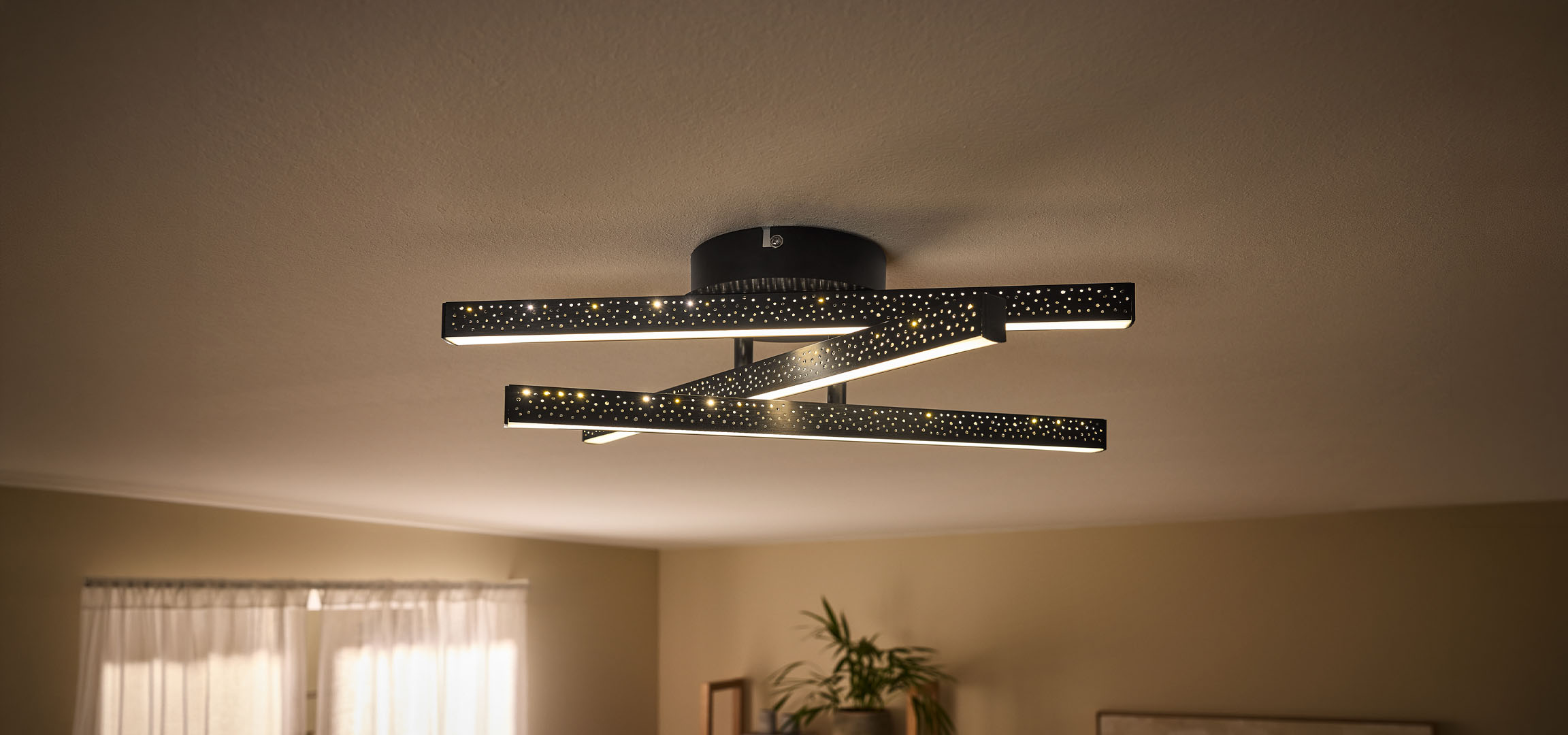 Modern LED-taklampa med svarta, perforerade stänger och varmt ljus.