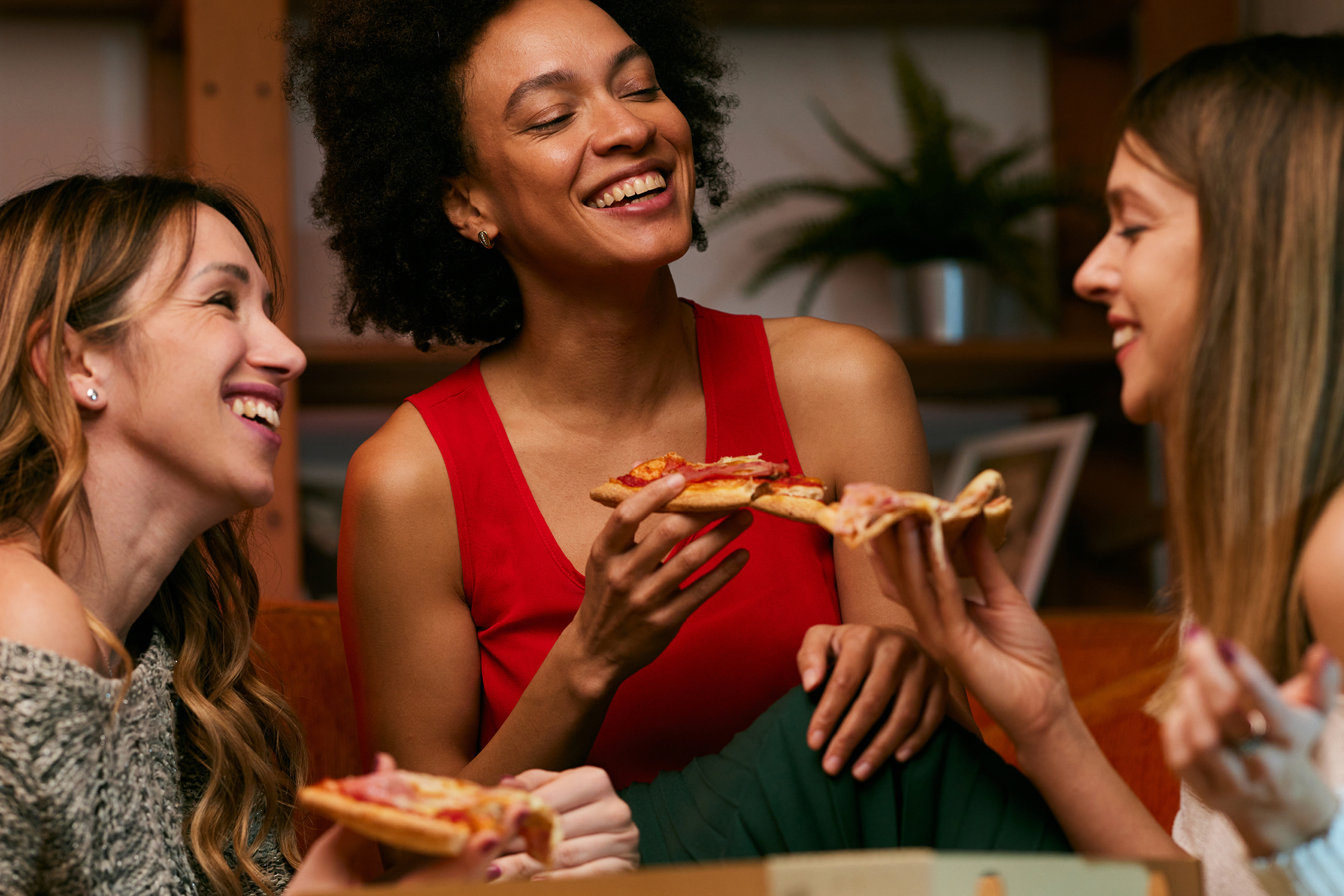 Tre glada kvinnor äter pizza tillsammans.