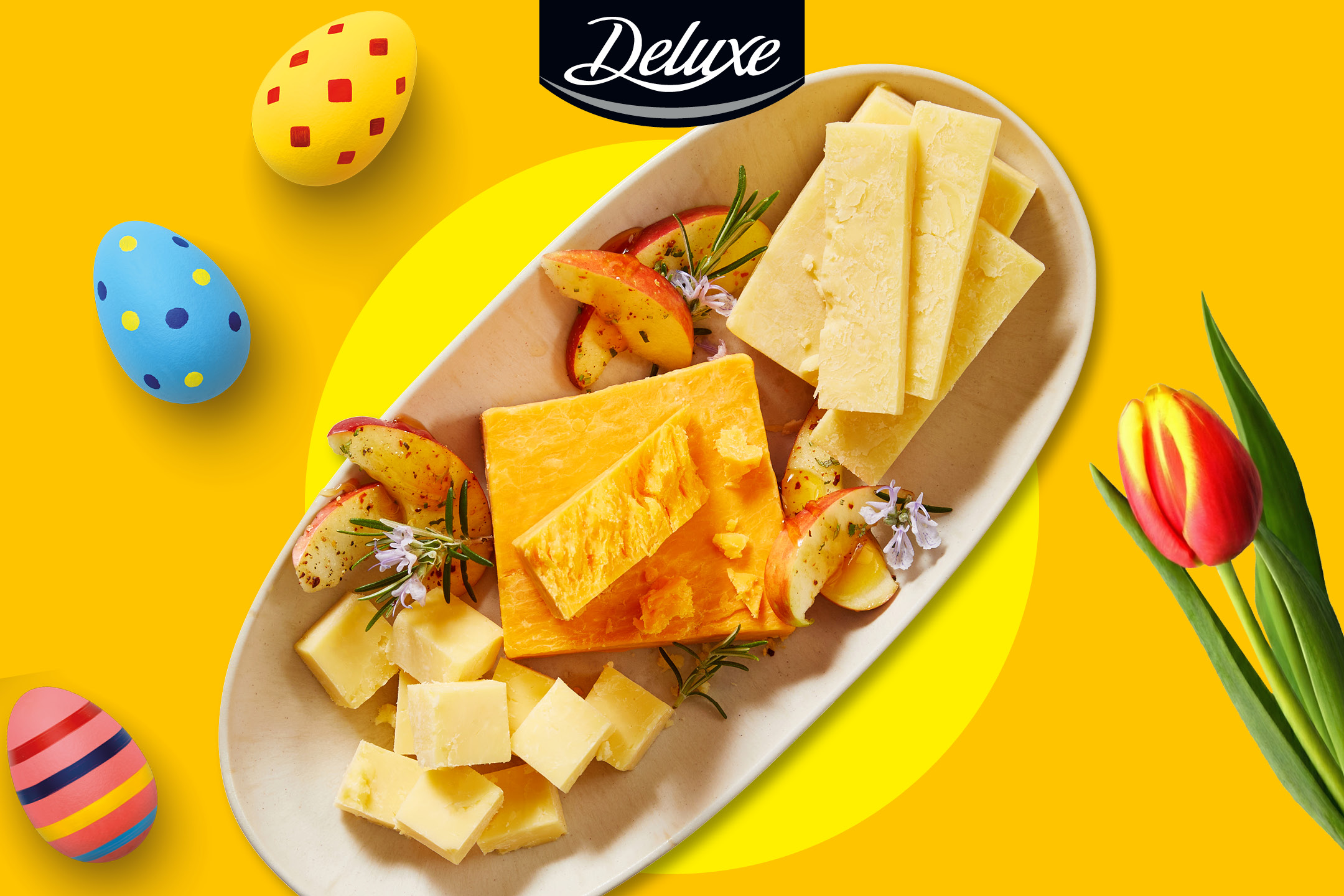 En ostbricka med äppelskivor och rosmarin, omgiven av påskägg och en tulpan.