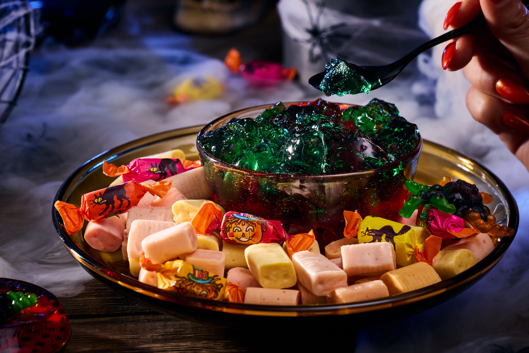 Halloween-godis med gelé och kolor på ett fat omgivet av rök.