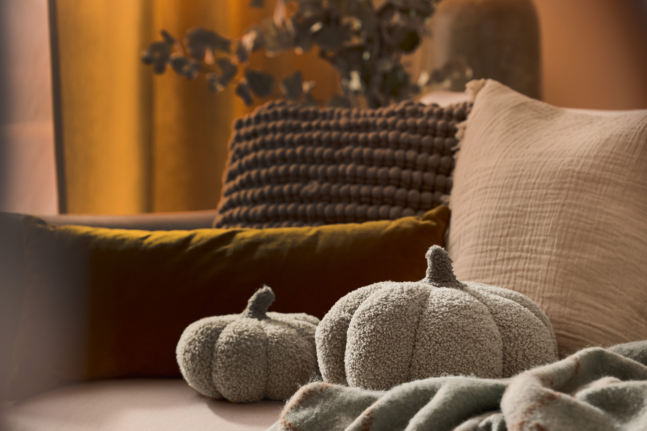 Två dekorativa tygpumpor i teddytyg, en gul kudde och en beige filt.