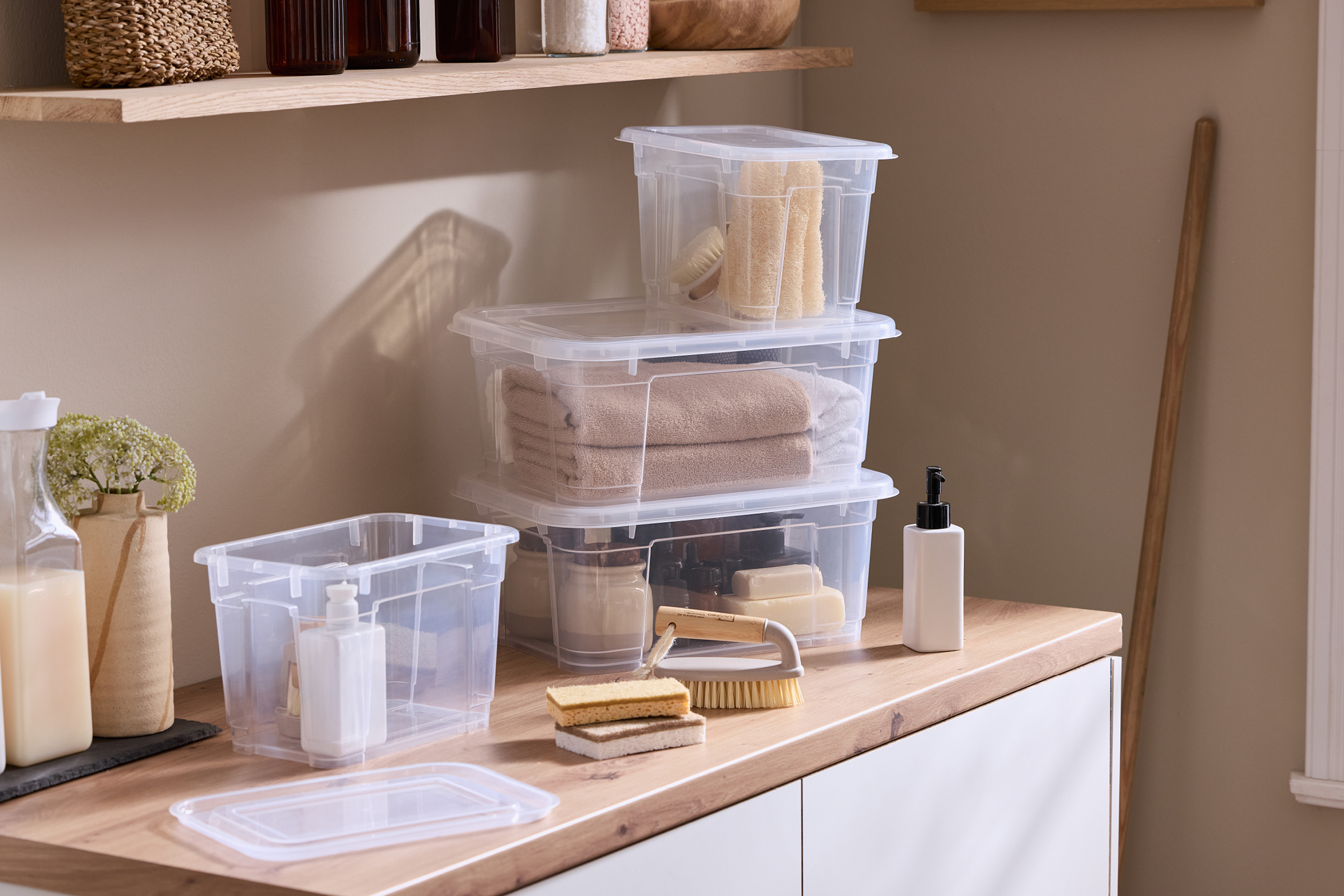 Transparenta förvaringslådor med handdukar, tvål och badtillbehör på en träbänk.