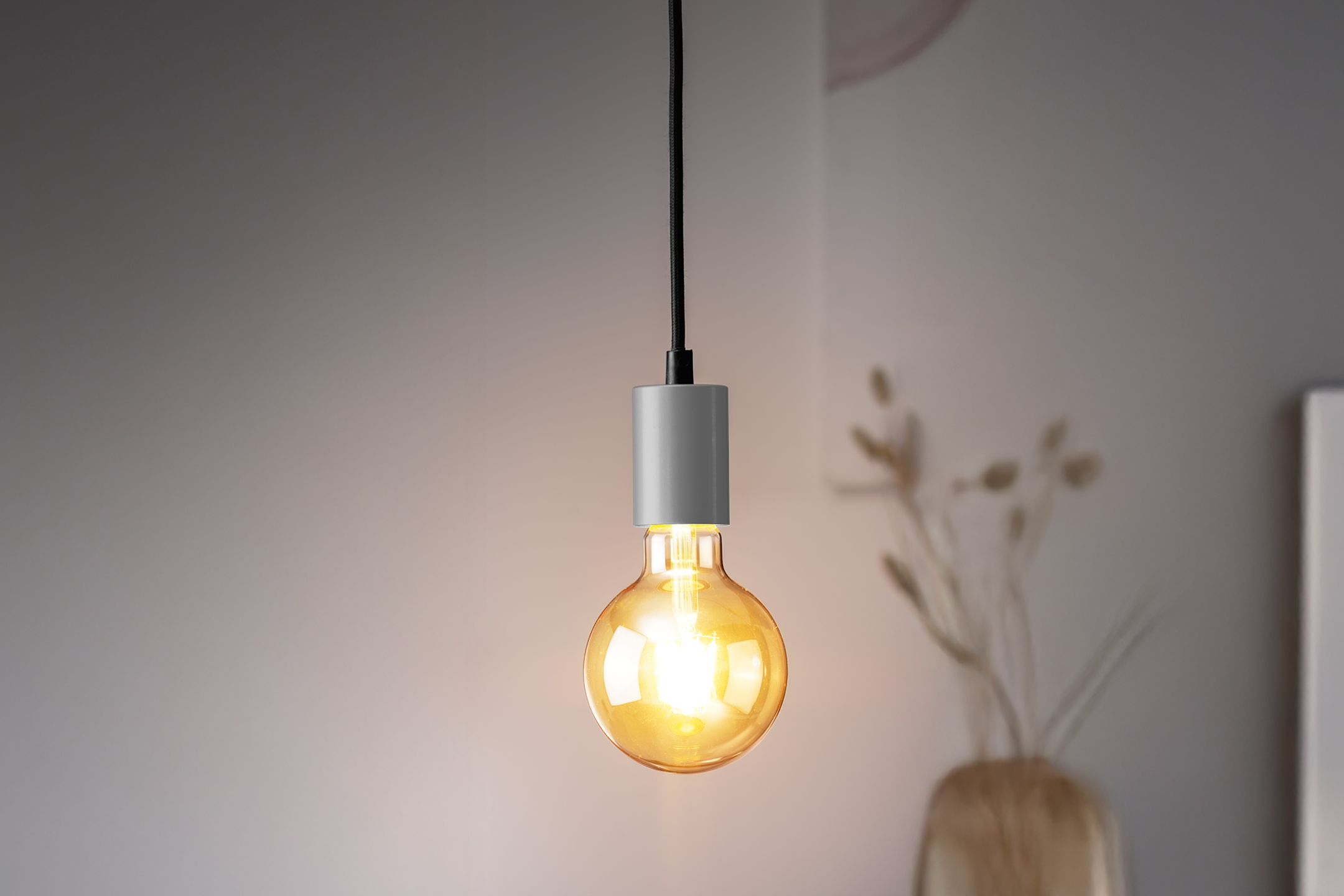 En glödande Edison-lampa hänger från taket, med en vas med torkade växter i bakgrunden.