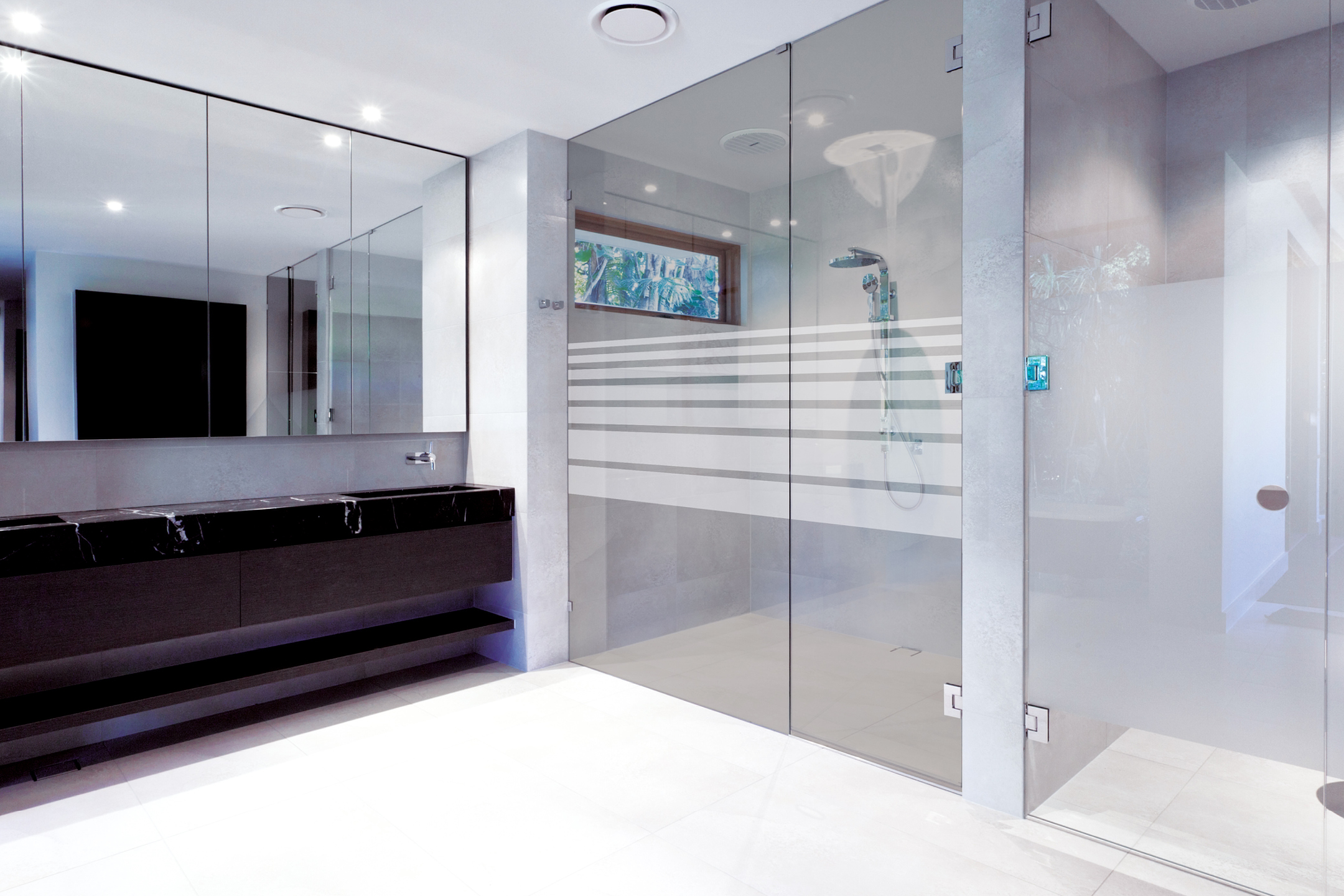 Modernt badrum med svart marmorbänk, spegelskåp och dusch med glasvägg.