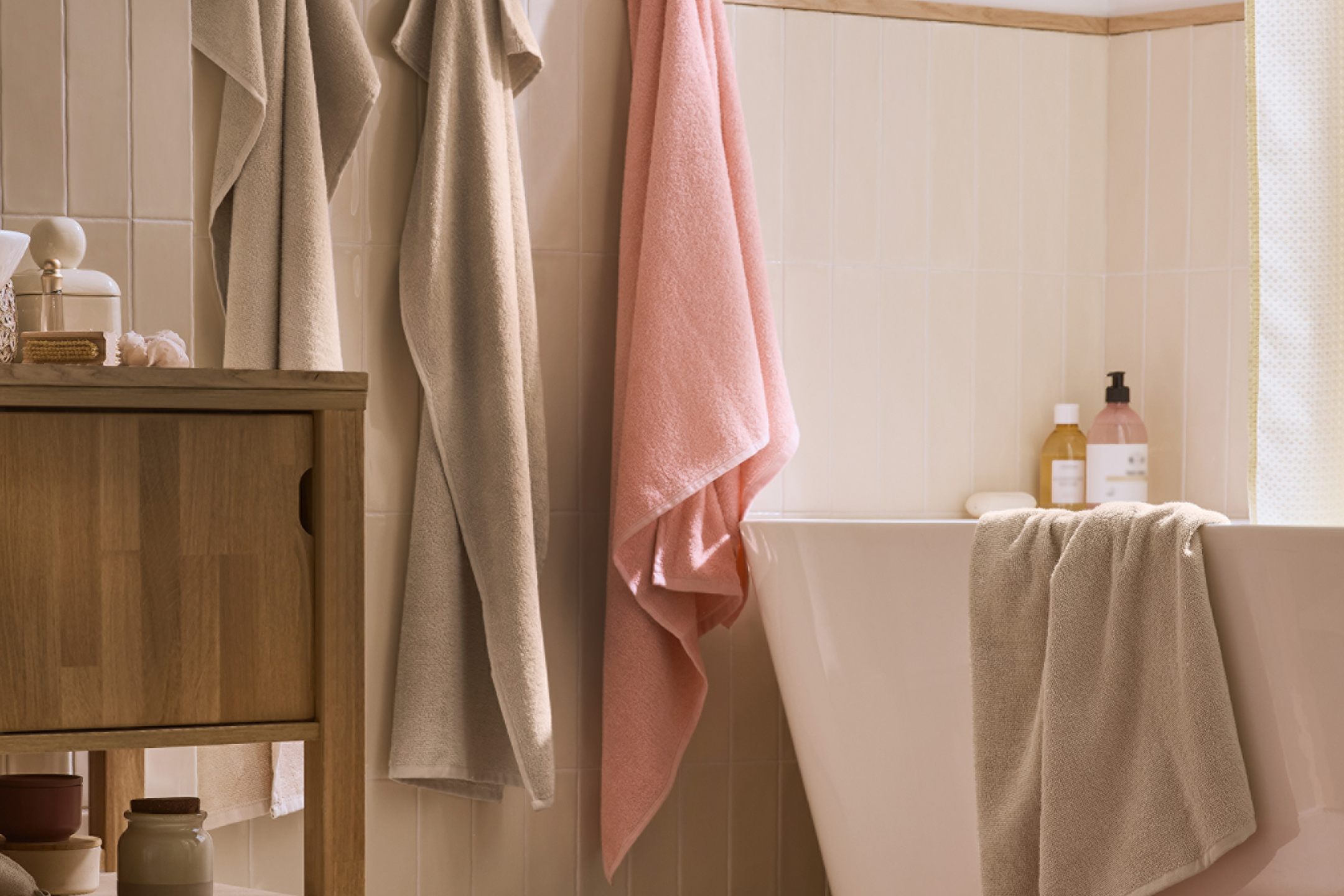 Badrum med handdukar i beige och rosa, badkar och träskåp.