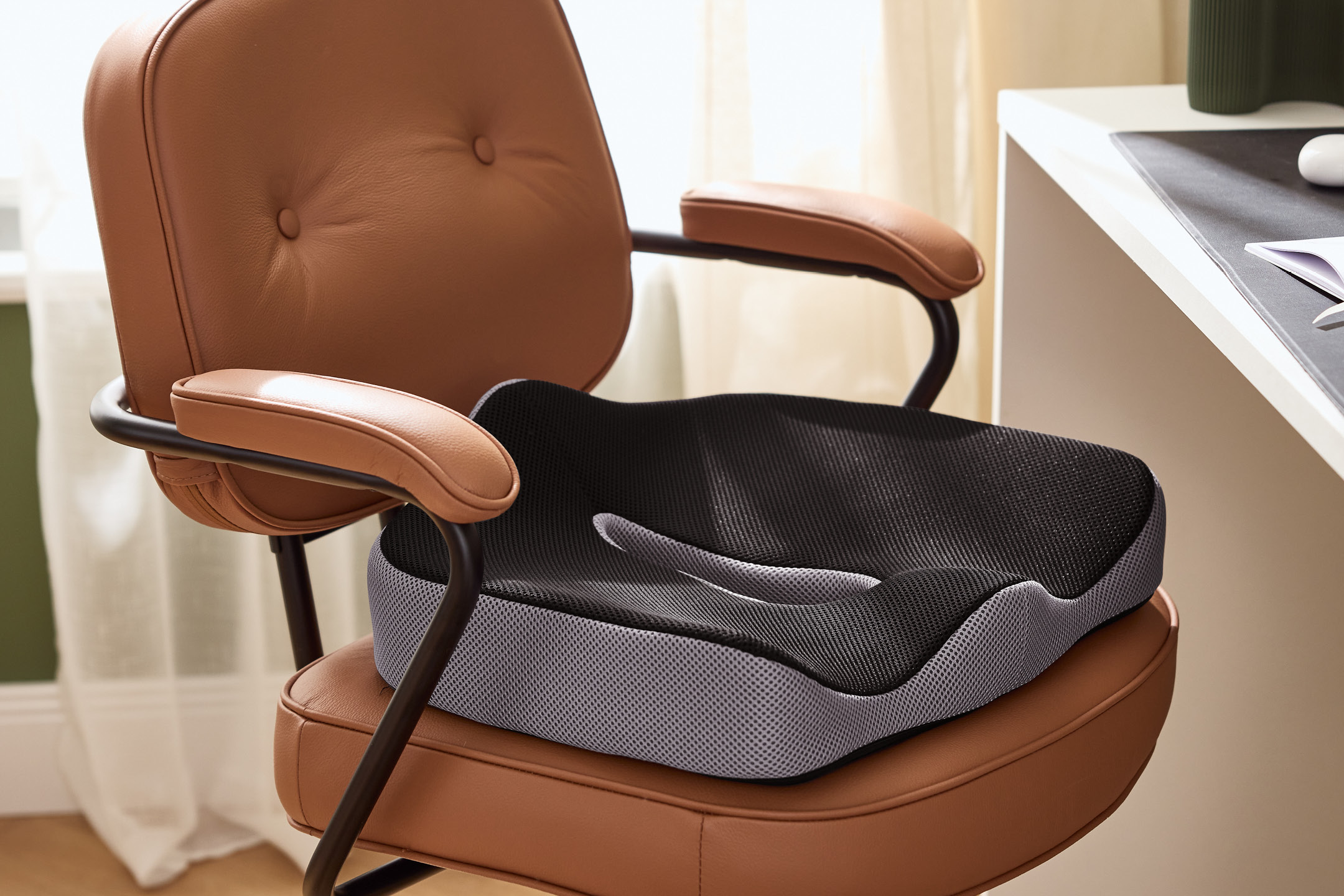 Ergonomisk sittdyna i svart och grått mesh på en brun kontorsstol vid ett skrivbord.