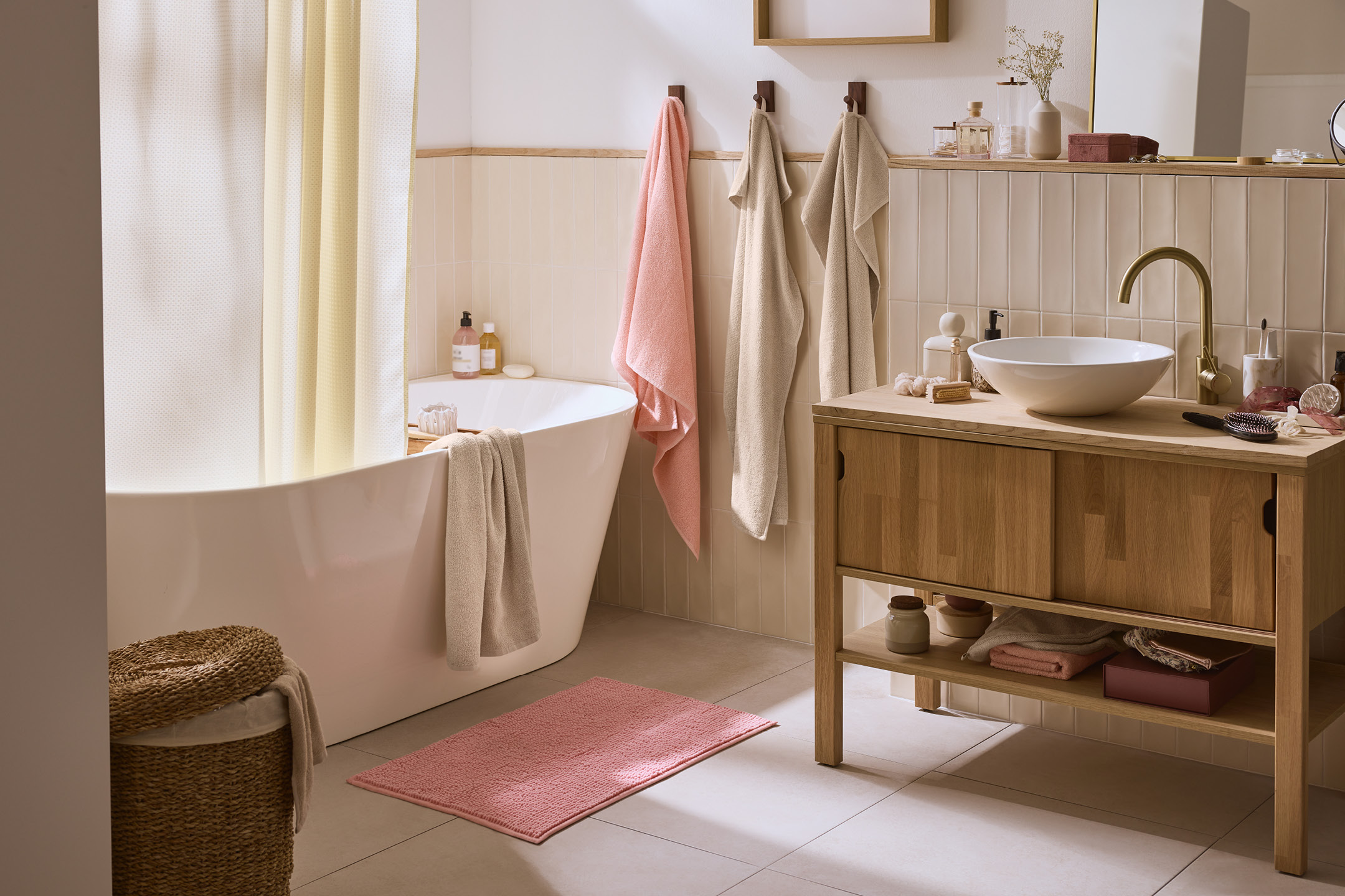 Badrum med badkar, duschdraperi, handdukar, badrumsmatta och tvättställ med kommod.