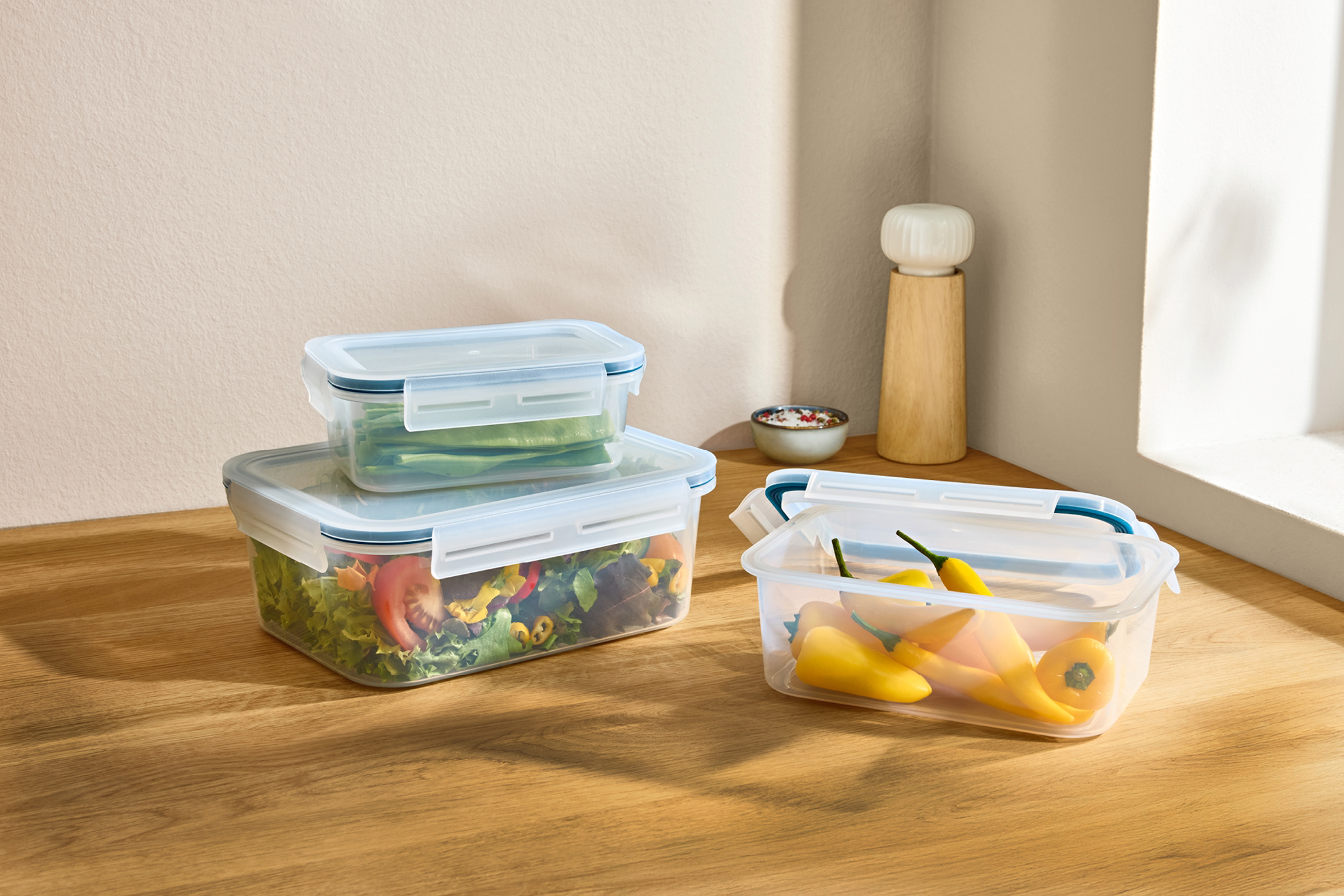 Matlådor med sallad, gröna bönor och gula paprikor på en träbänk.