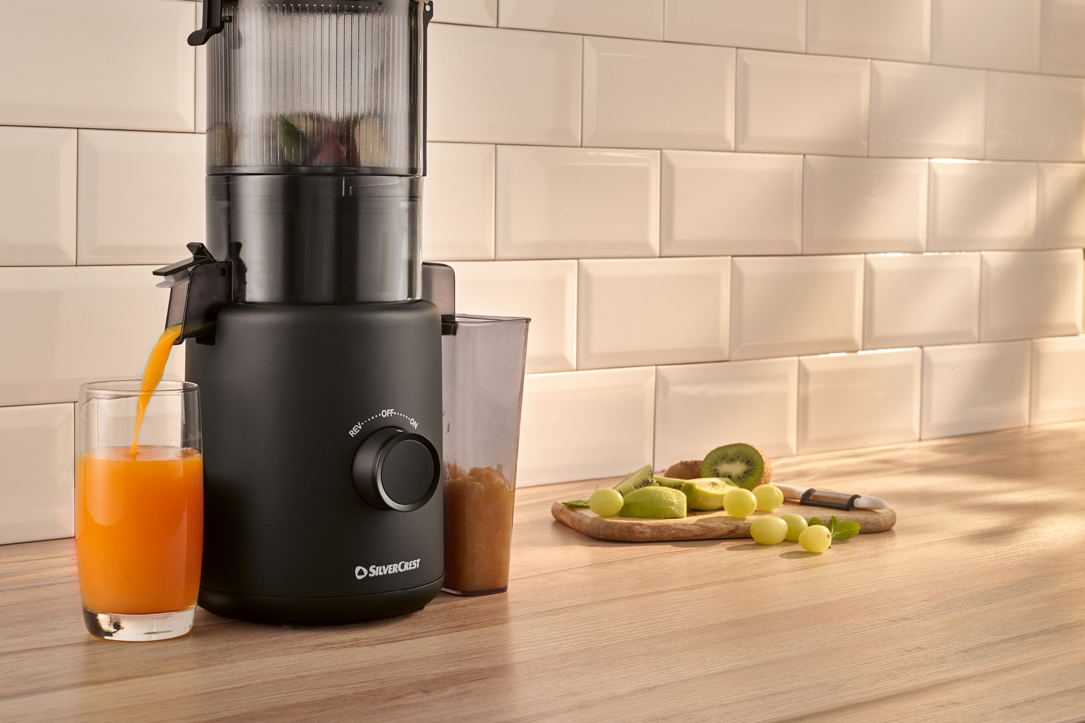 Svart slowjuicer som pressar apelsinjuice i ett glas, med frukt på en träskärbräda.