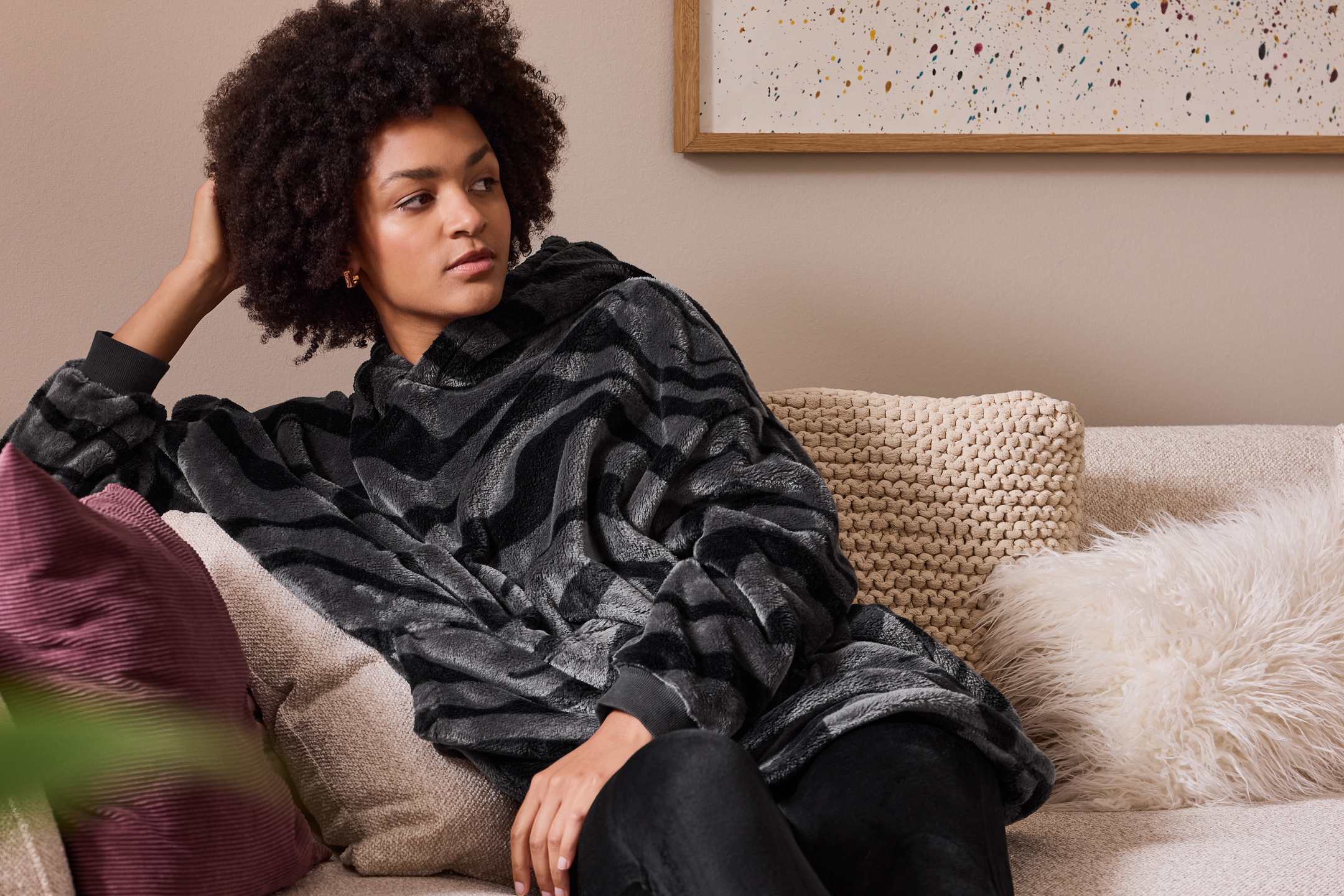 Kvinna i mysig svart och grå filttröja med zebratryck, sitter i soffa med kuddar.