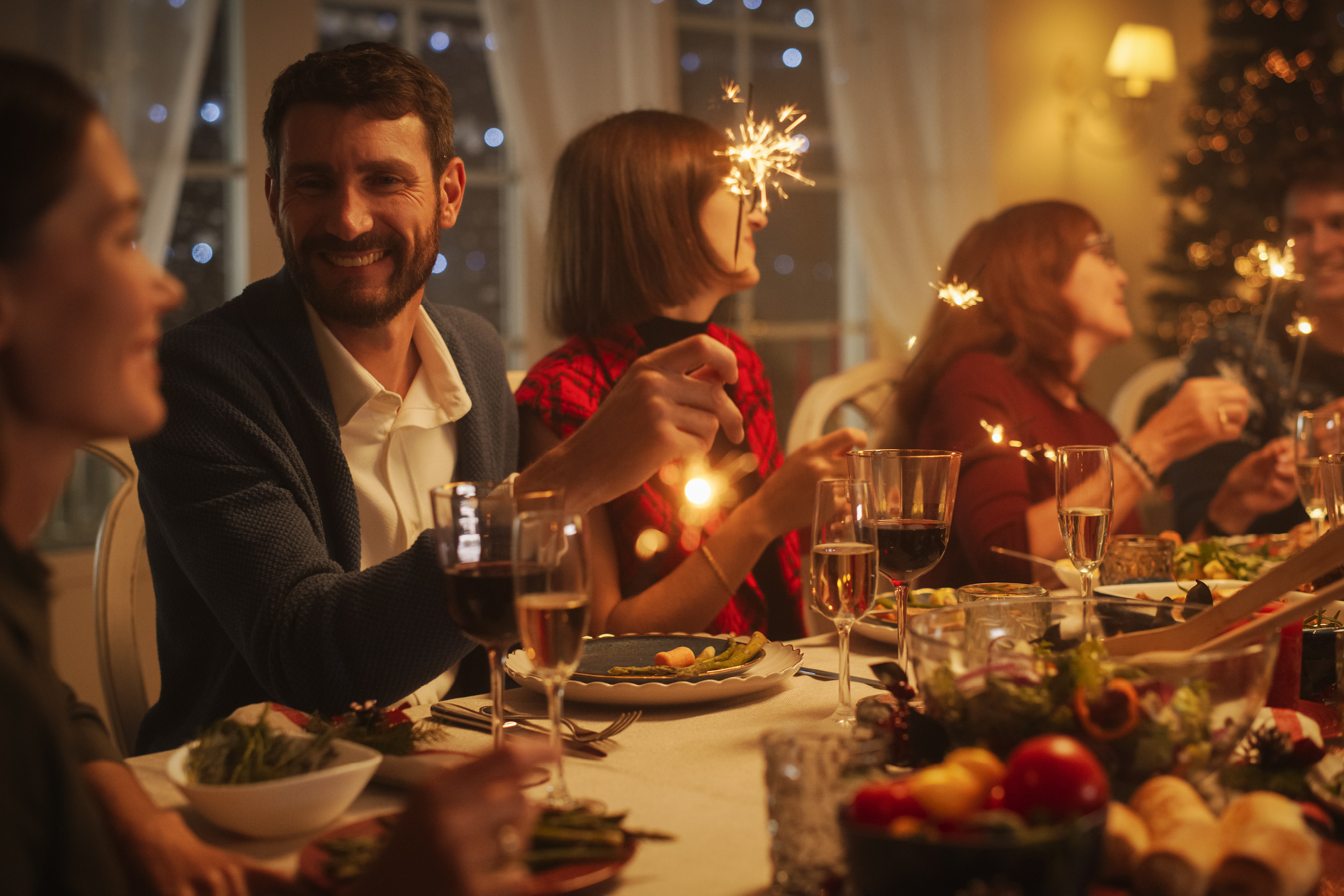 Människor firar julmiddag med gnistrande tomtebloss och mat på bordet.