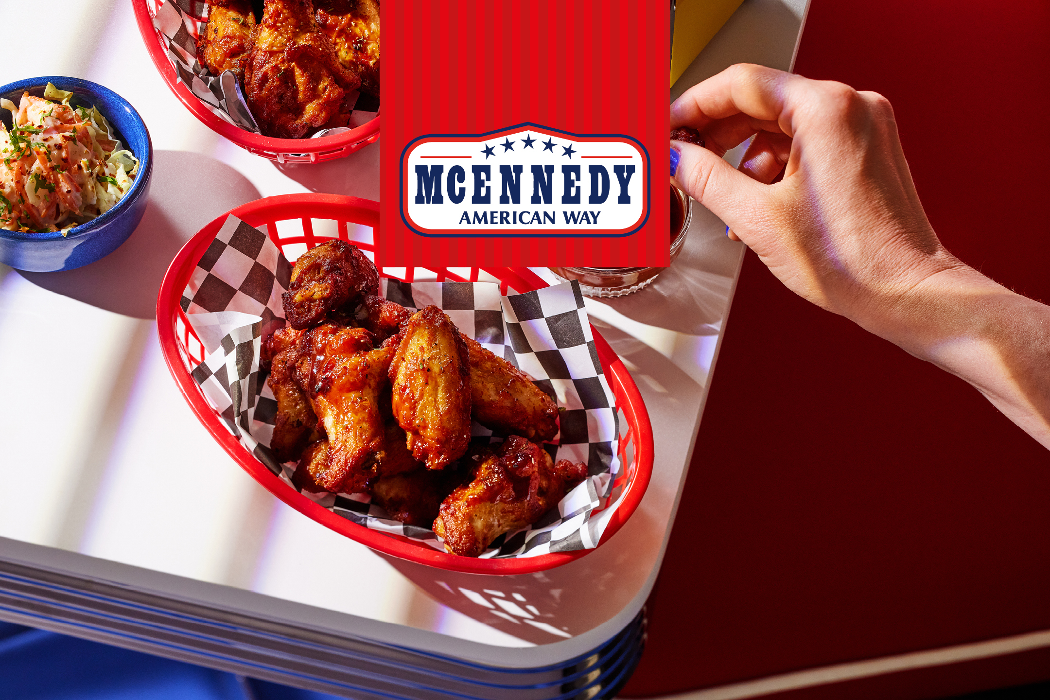 Friterade kycklingvingar i röda korgar med coleslaw och en hand som doppar en vinge.