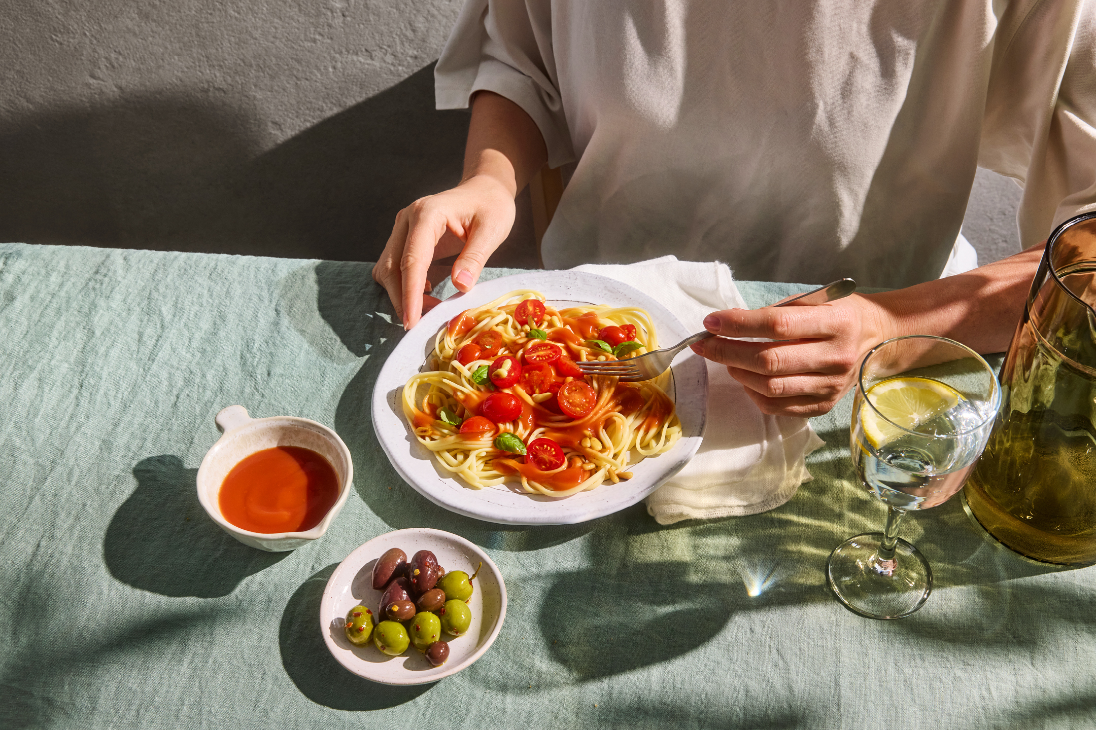 En person äter spaghetti med tomatsås, körsbärstomater och basilika, med oliver och vatten.