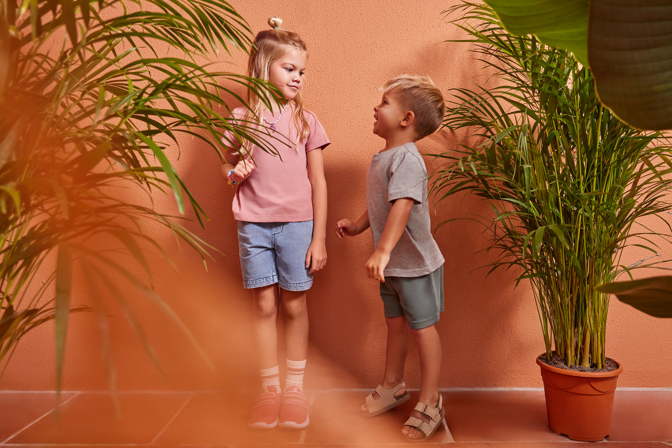 Två barn i sommarkläder, en flicka i rosa t-shirt och jeansshorts, en pojke i grå t-shirt och shorts.