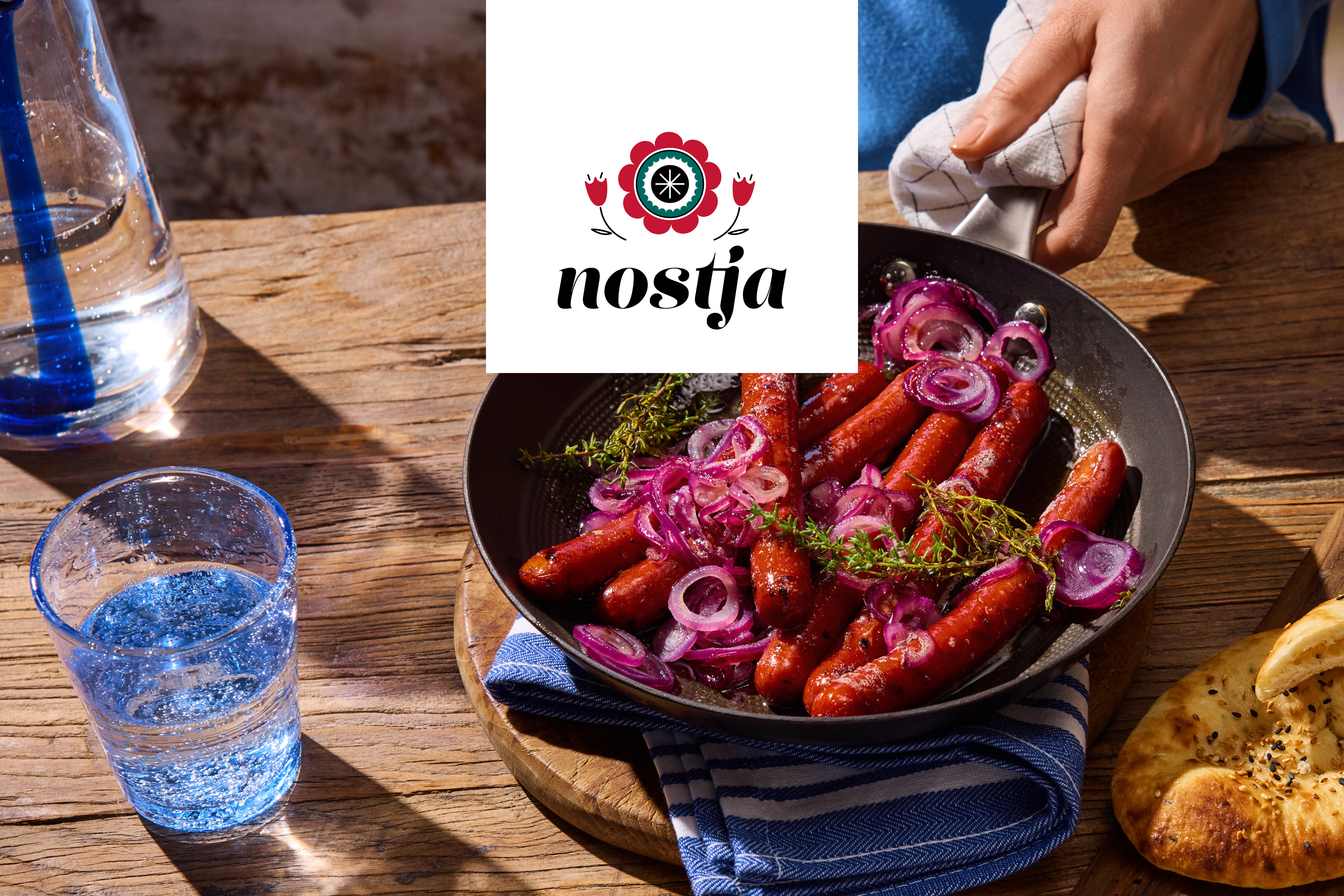 Stekta korvar med rödlök och timjan i en panna, med vatten och bröd på ett träbord.