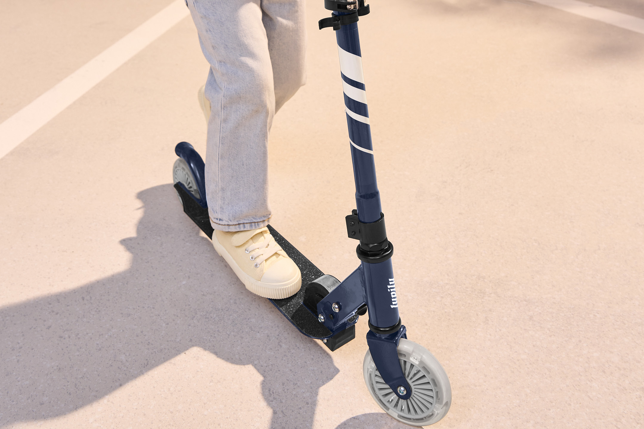 Ett barn på en mörkblå sparkcykel med vita ränder och ljusa hjul.