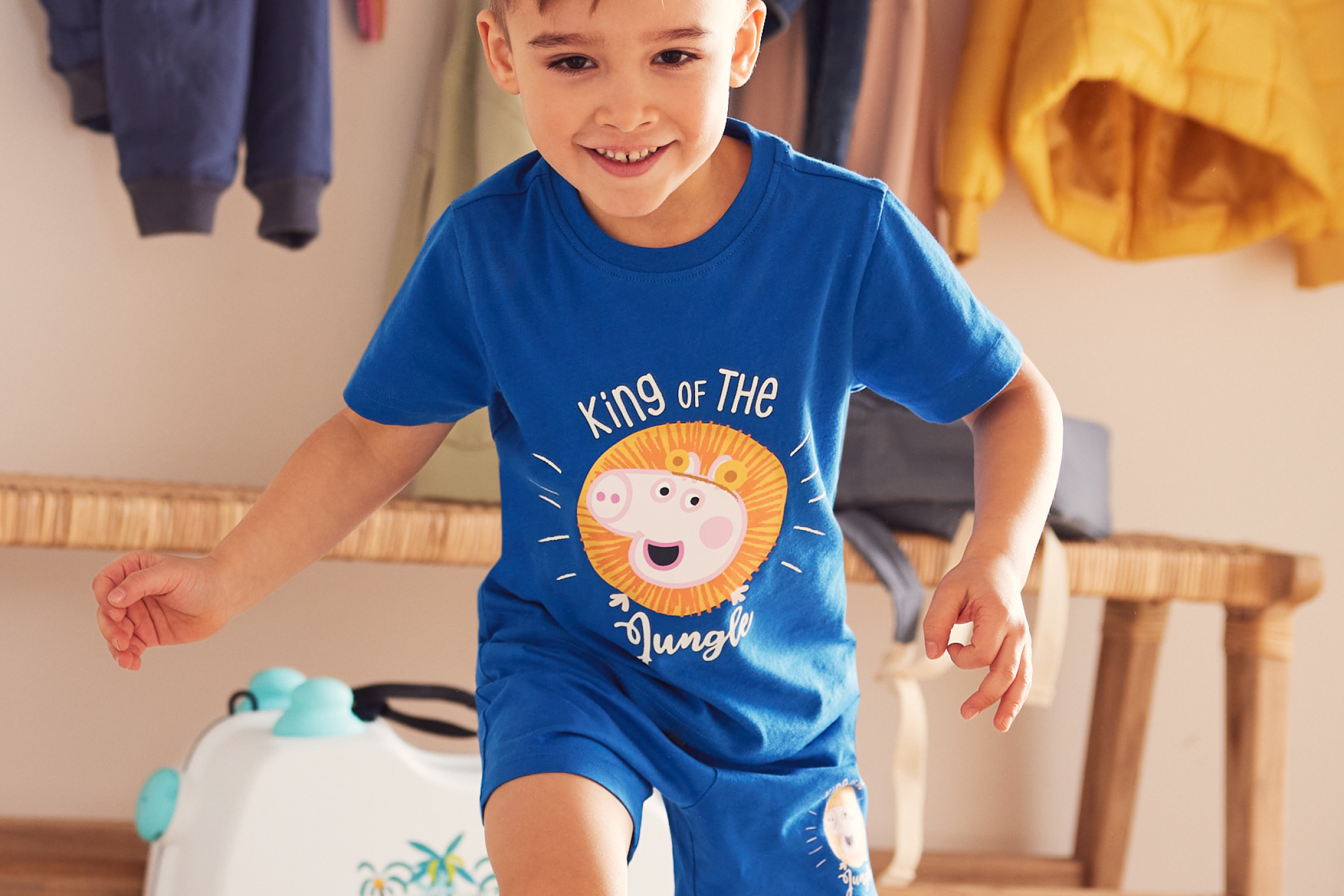 Glad pojke i blått t-shirt och shorts med Peppa Pig-lejonmotiv och texten 'King of the Jungle'.