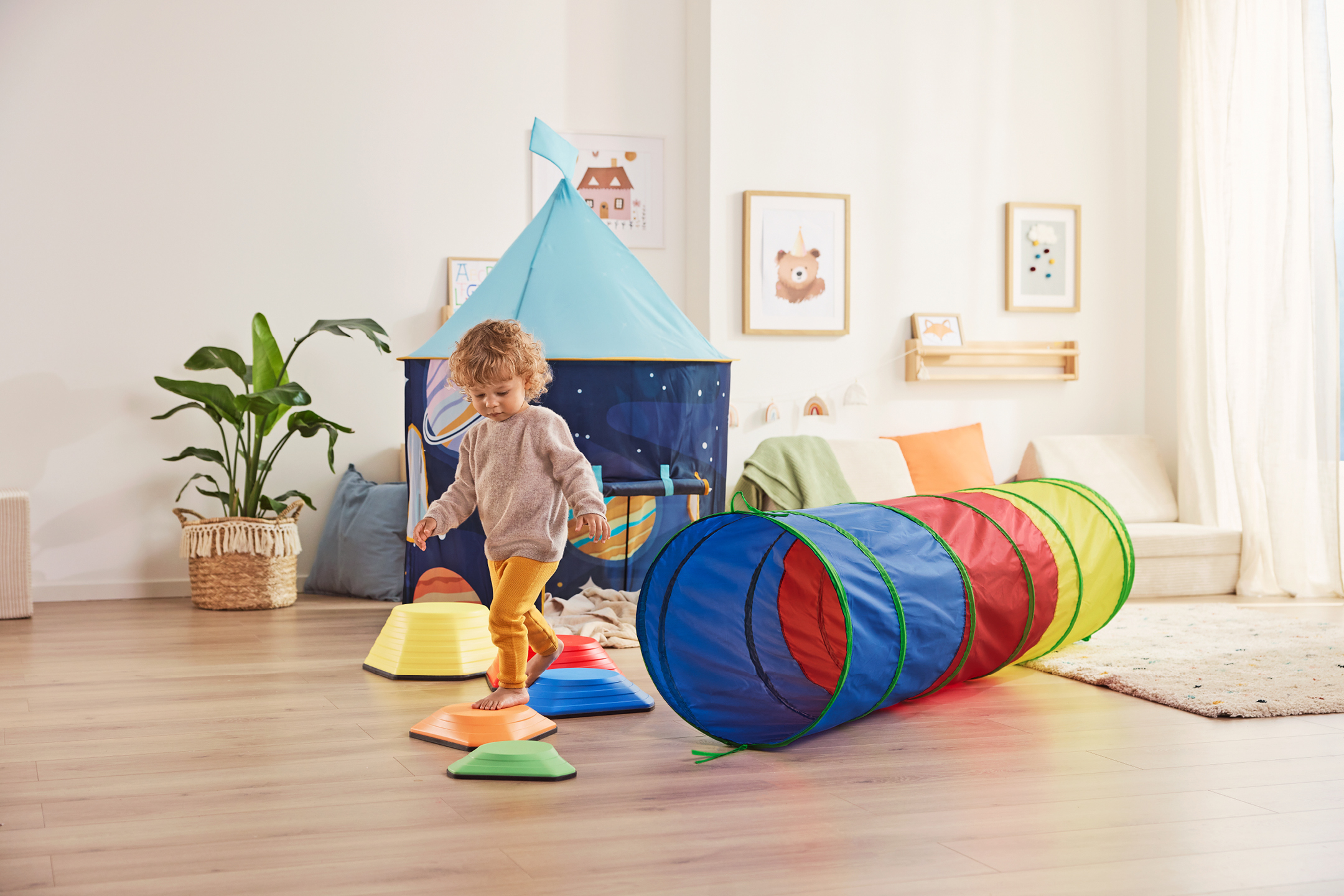 Ett barn leker med en färgglad lektunnel och balansstenar i ett barnrum.