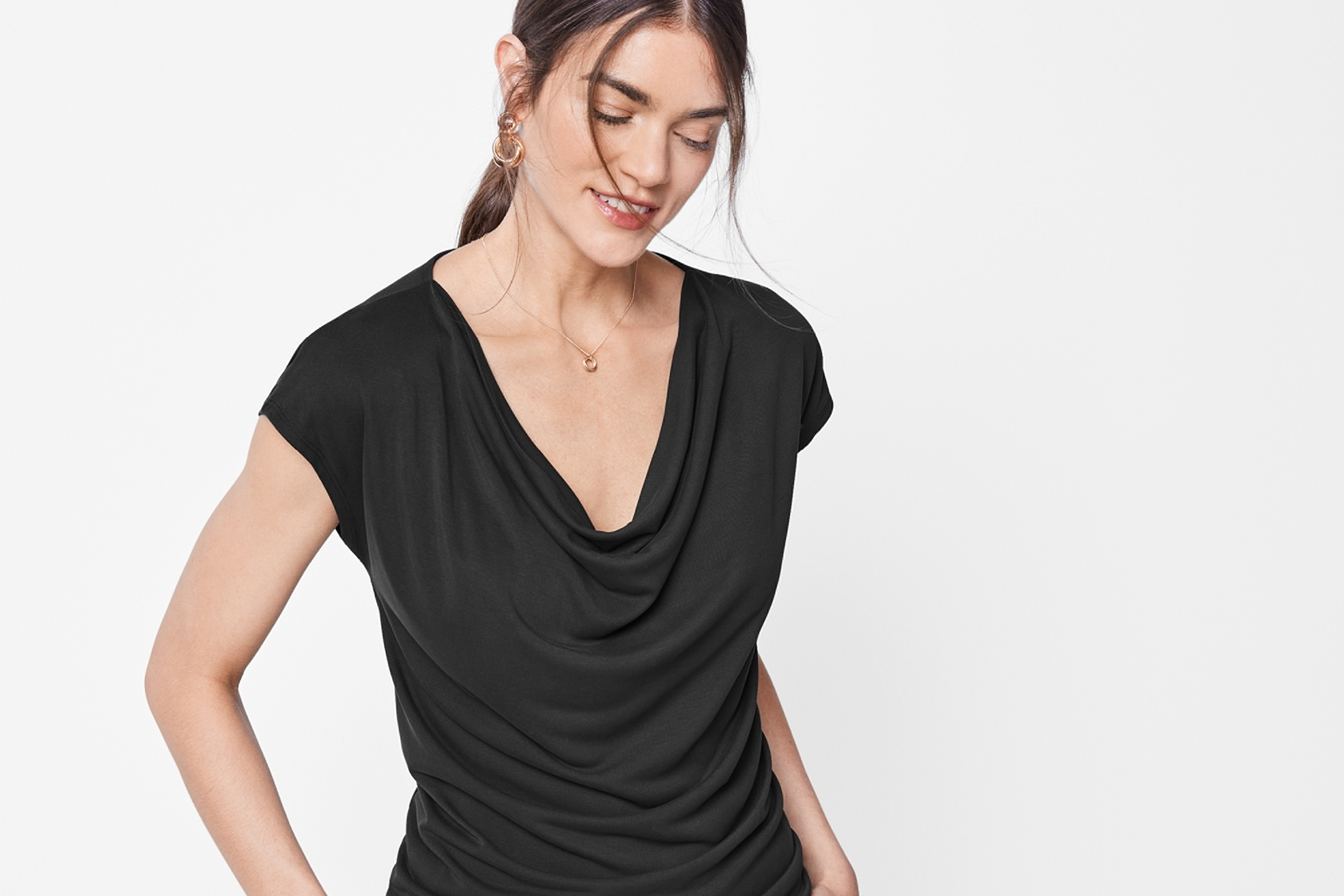 Kvinna i svart topp med draperad halsringning och guldhalsband.