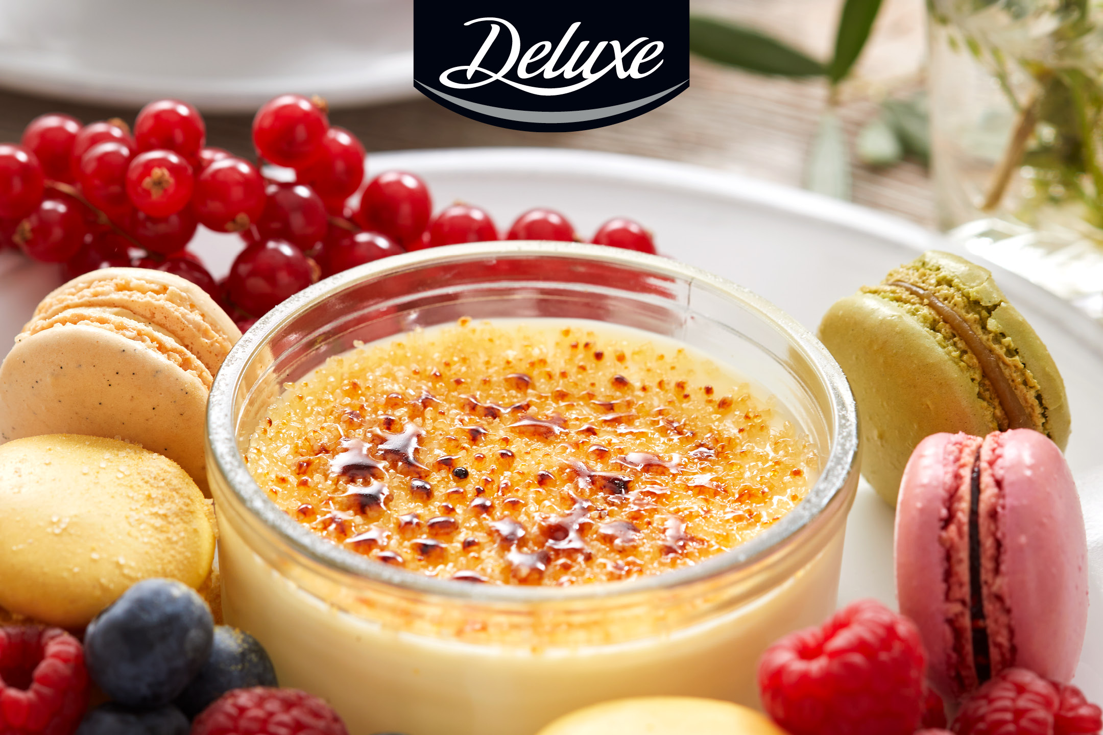 Crème brûlée med makaroner, röda vinbär, hallon och blåbär på en vit tallrik.