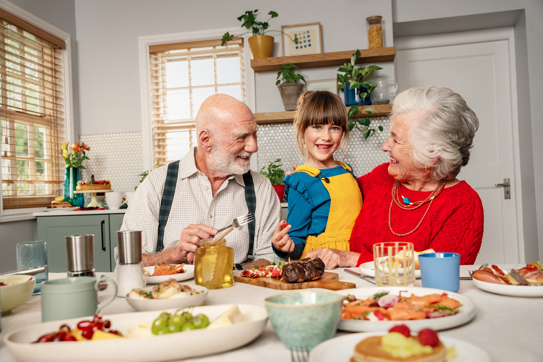 Glada morföräldrar och barnbarn vid ett frukostbord med olika rätter.