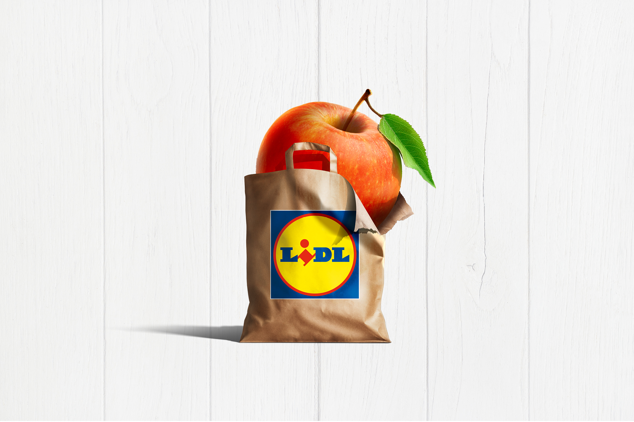 Ett stort rött äpple sticker upp ur en brun papperspåse mot en vit träbakgrund.