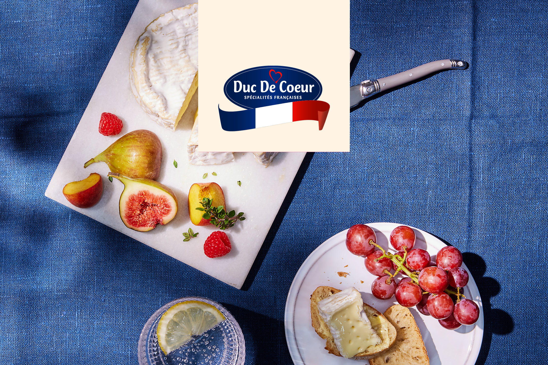 Fransk ostbricka med brie, fikon, hallon, persika, vindruvor och bröd på en blå duk.