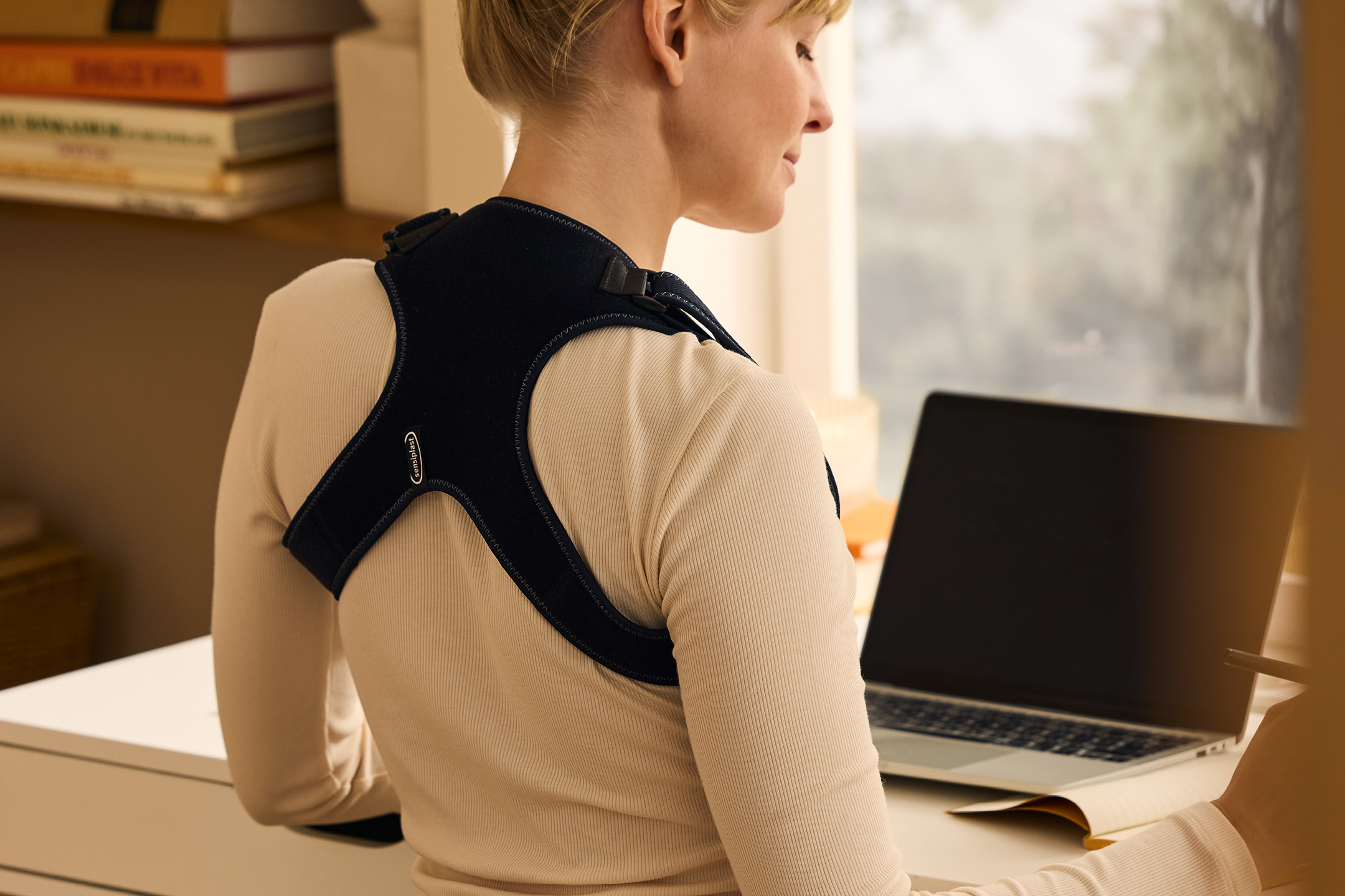 Kvinna med hållningskorrigerare arbetar vid ett skrivbord med en bärbar dator.