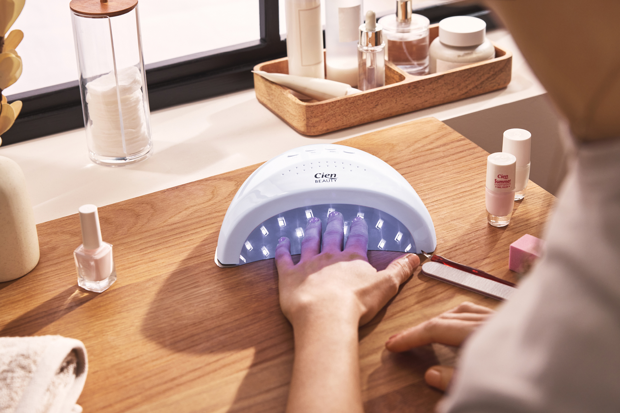 En person som använder en UV-lampa för naglar, med nagellack och bomullsrondeller i bakgrunden.