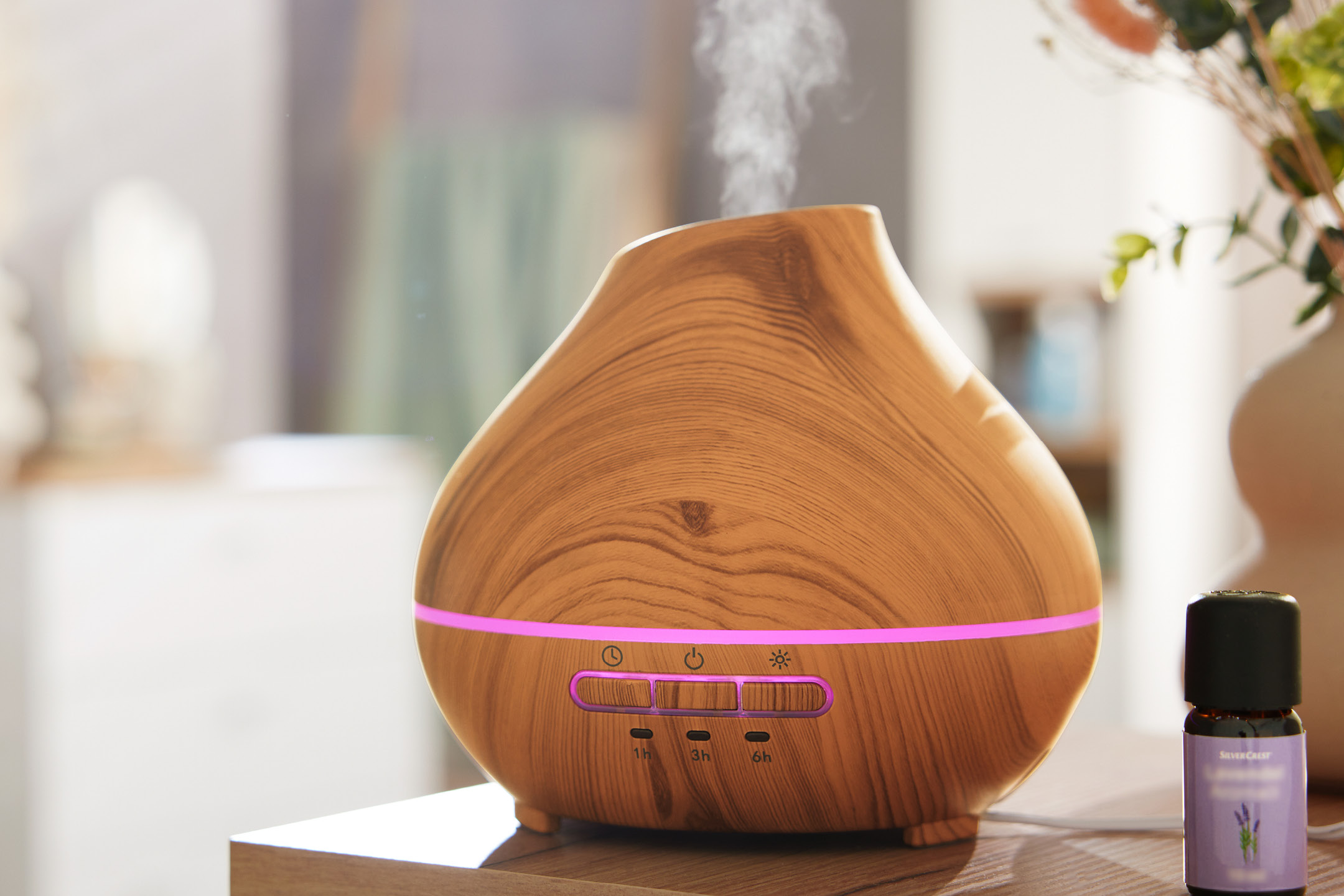 Träfärgad aromdiffuser med lila ljus och ånga, bredvid en flaska lavendelolja.