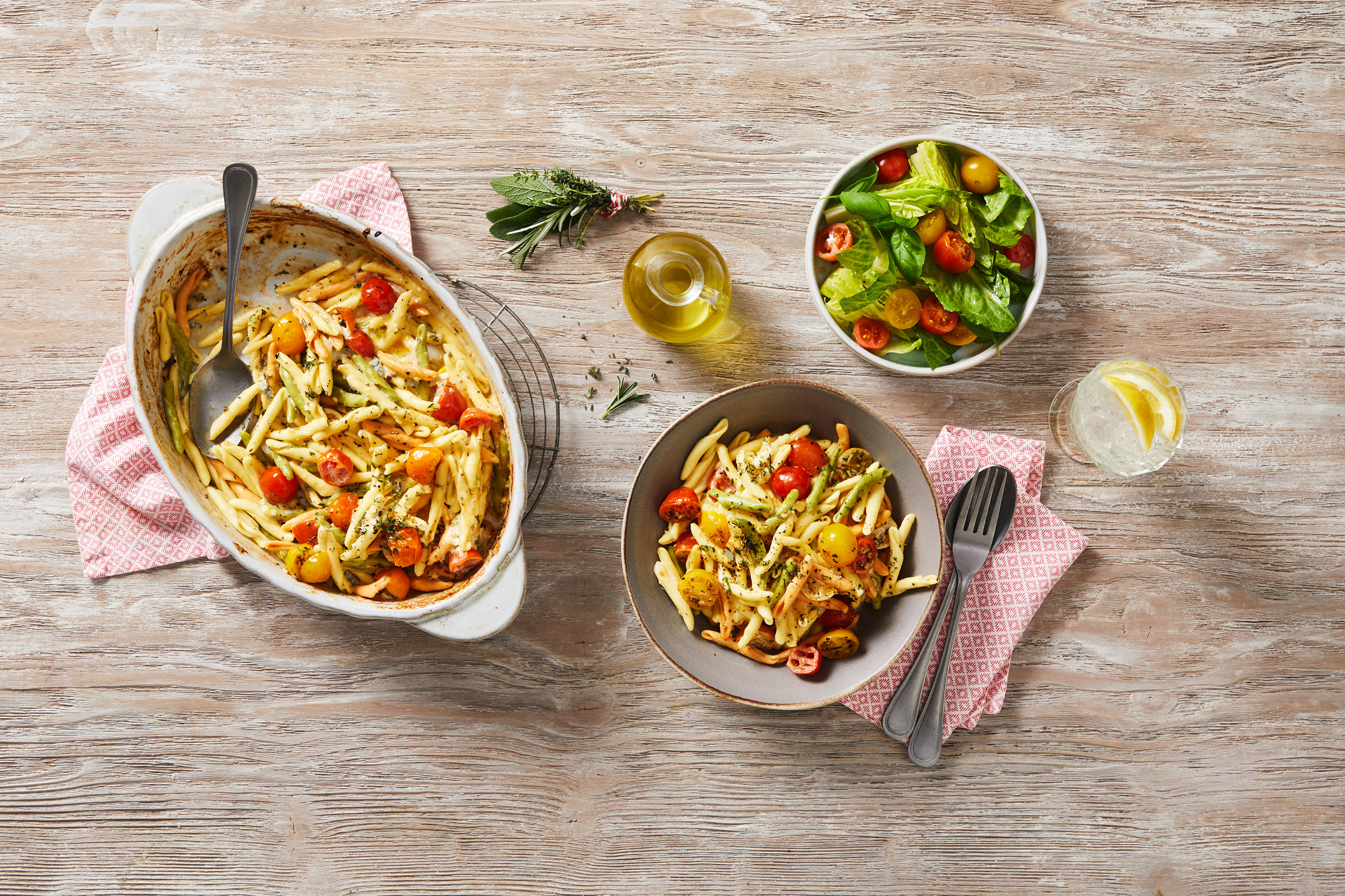 En gratängform och en tallrik med pasta, tomater och gröna bönor, med en sallad och dryck.