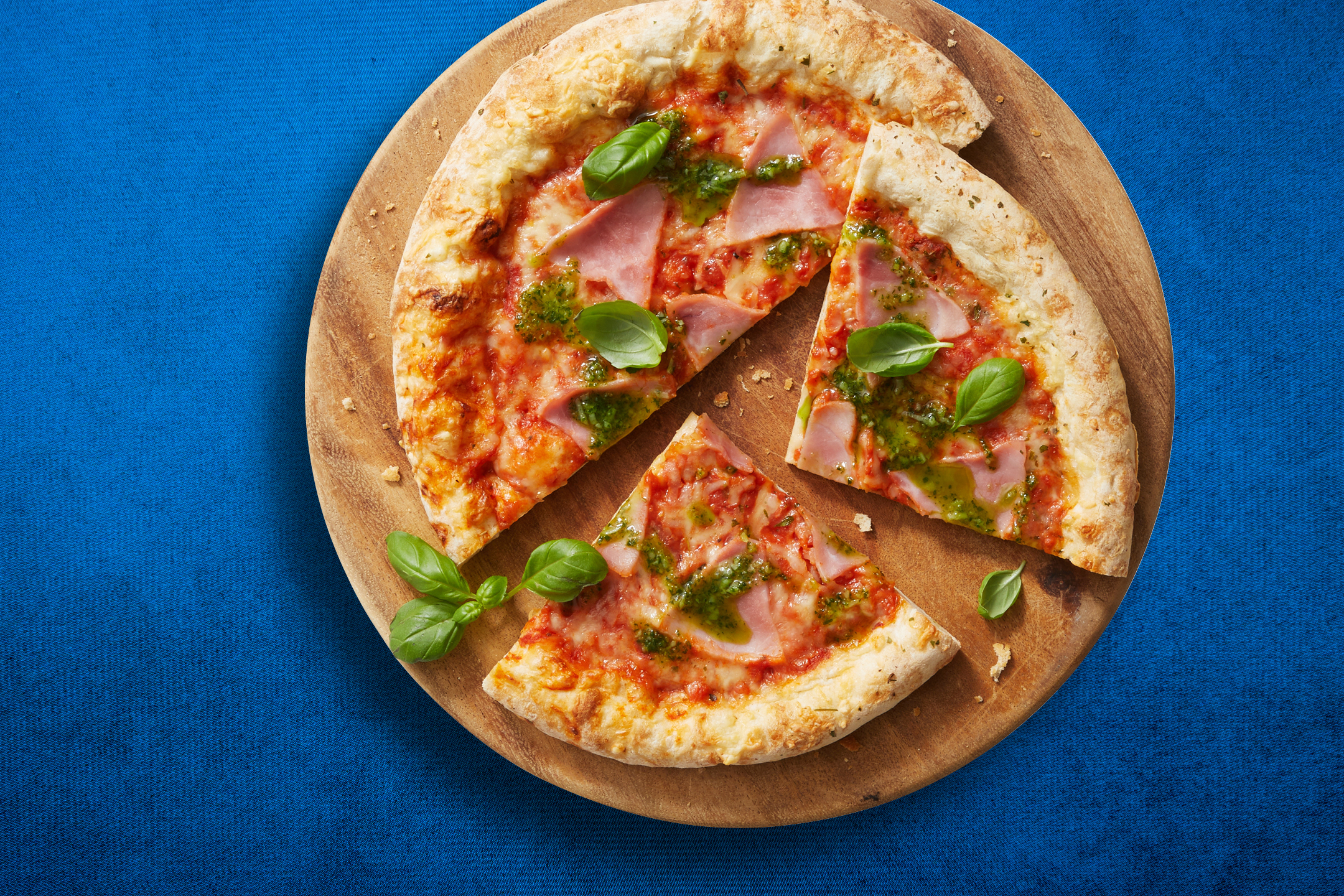 Pizza med skinka, pesto och basilika på en träskiva.