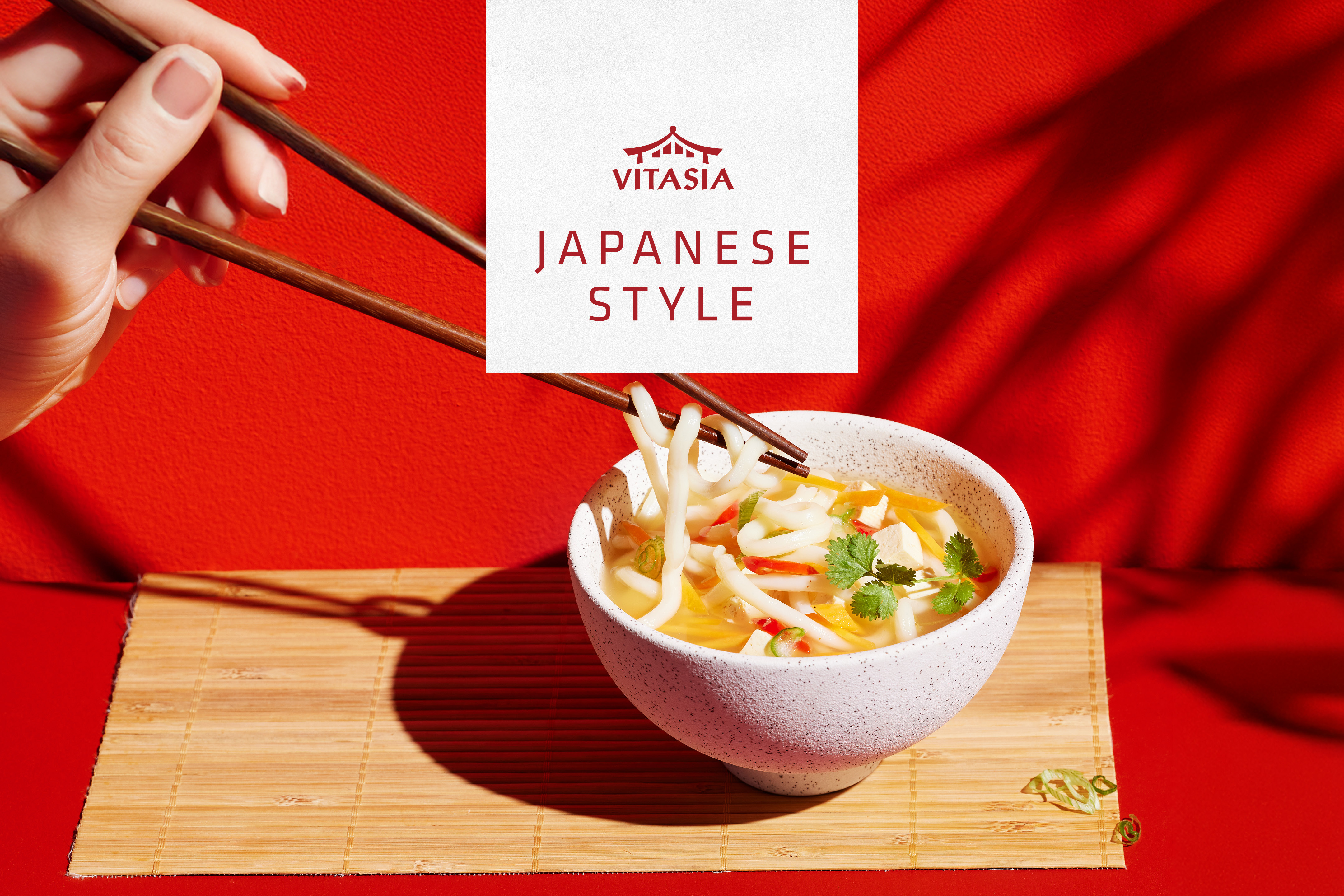 En hand med ätpinnar lyfter nudlar från en skål med japansk nudelsoppa.