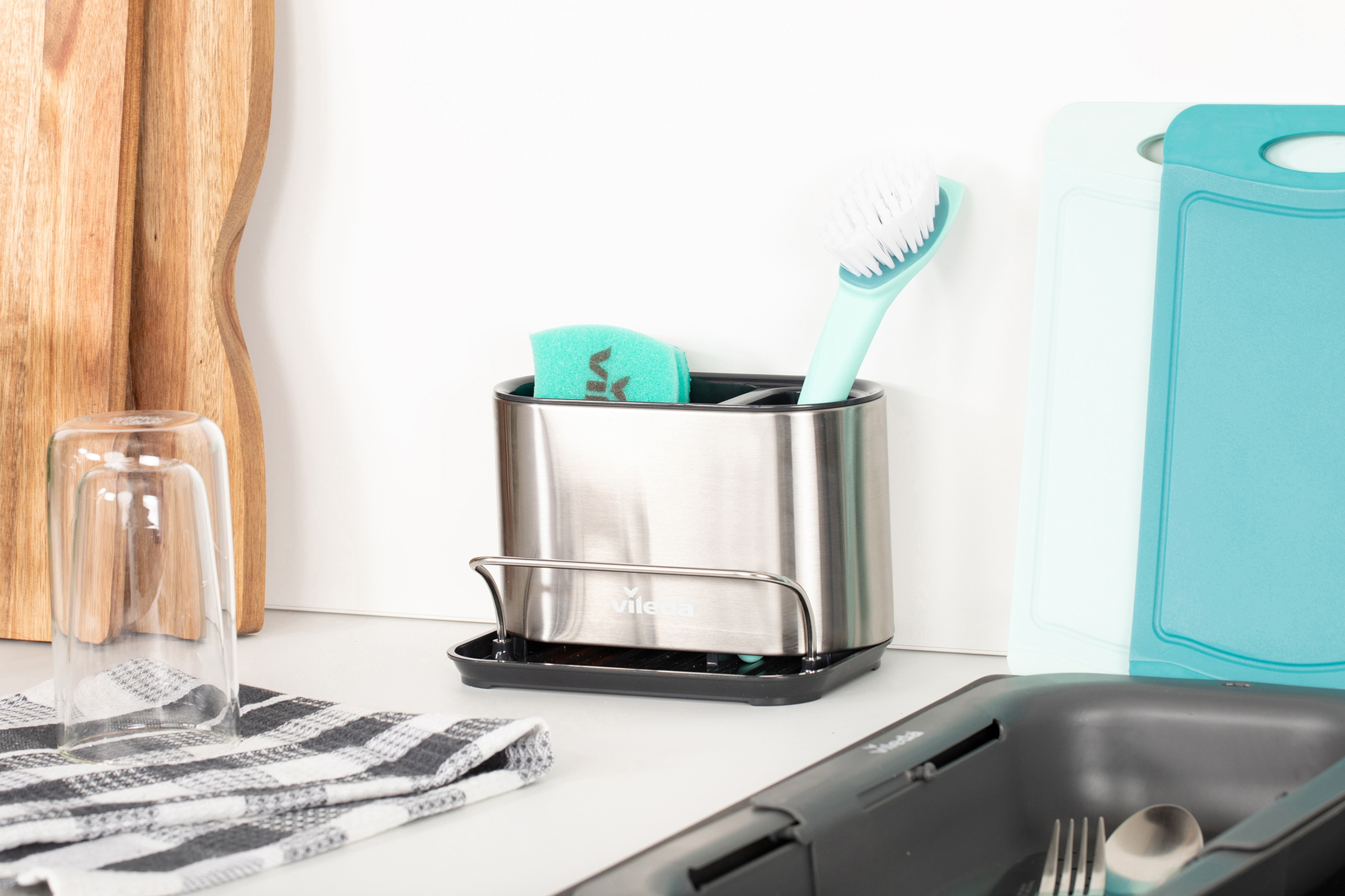 Diskställ i rostfritt stål med diskborste och svamp, bredvid skärbrädor och diskho.