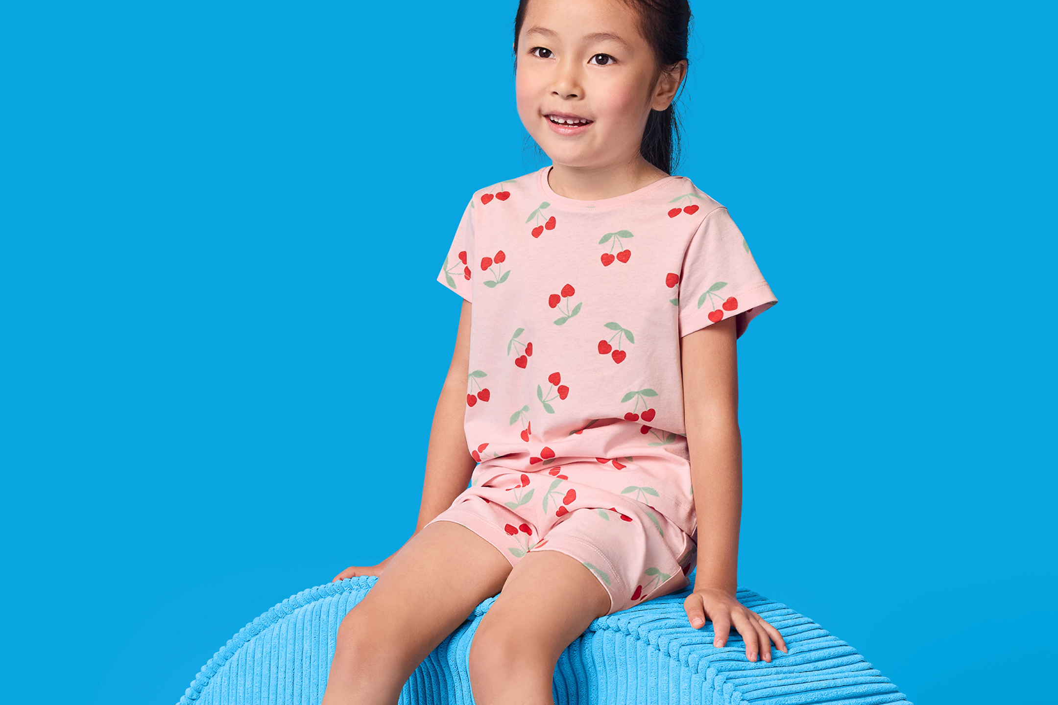 Flicka i rosa pyjamas med körsbärsmönster, sitter på en blå kudde.