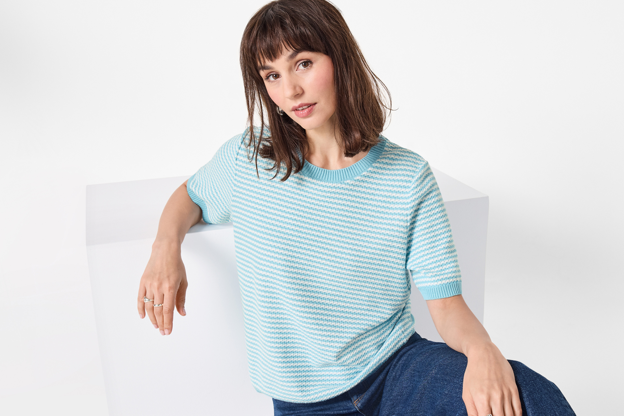 Kvinna i blåvitrandig tröja och jeans, sitter på en vit kub.