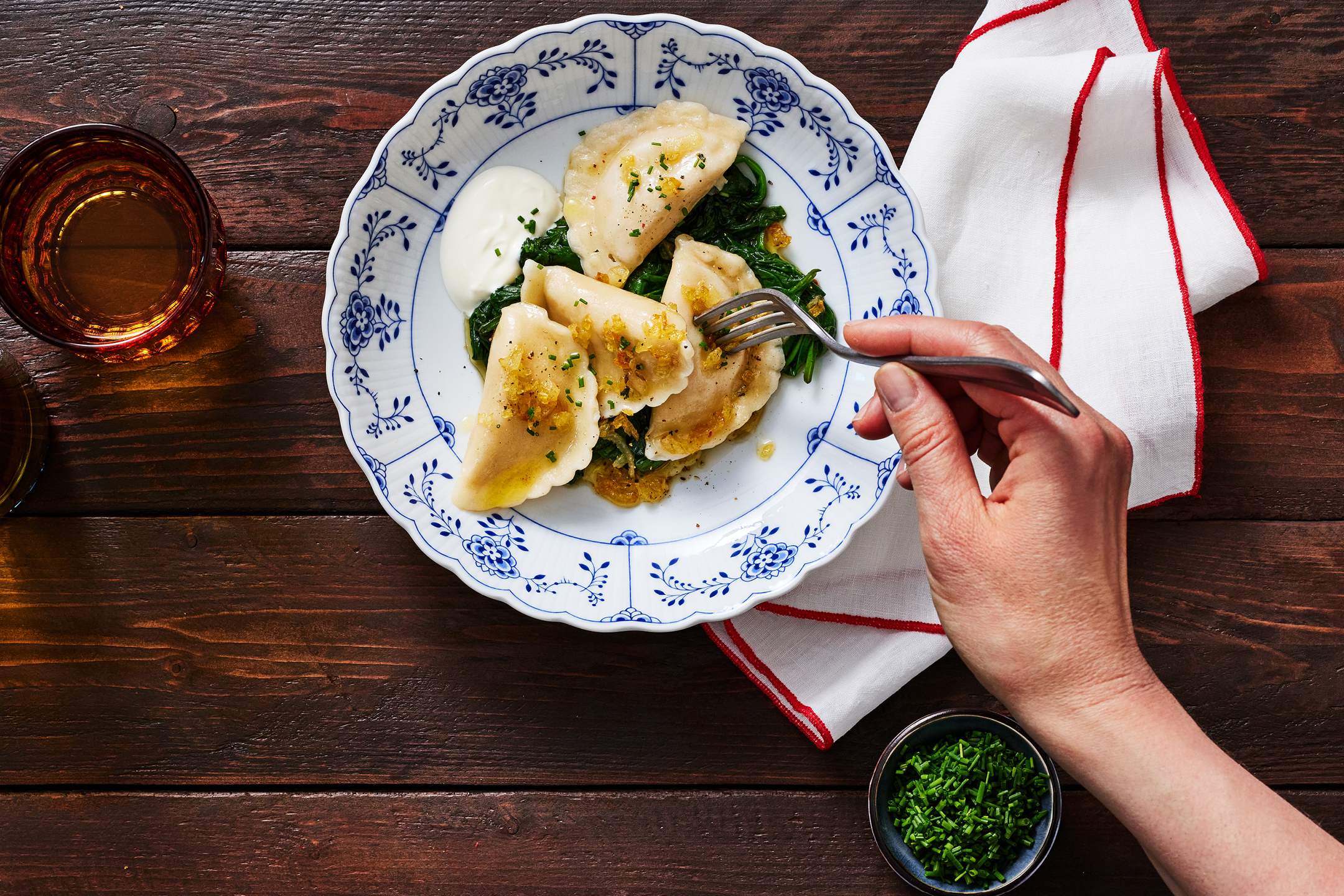 Hand som tar en dumpling från en tallrik med dumplings, spenat och gräddfil.