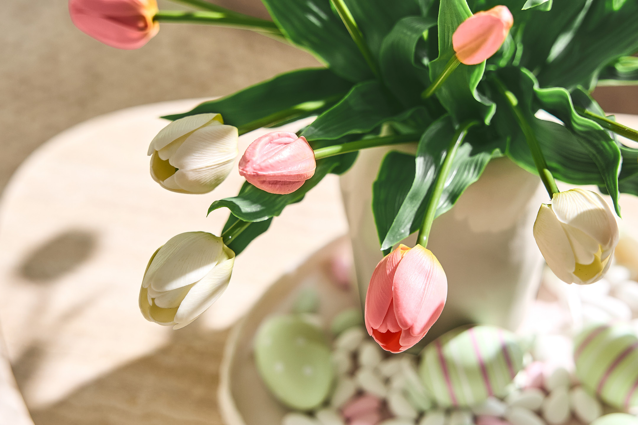 En bukett med rosa och vita tulpaner i en vas, med påskägg och godis på ett fat.