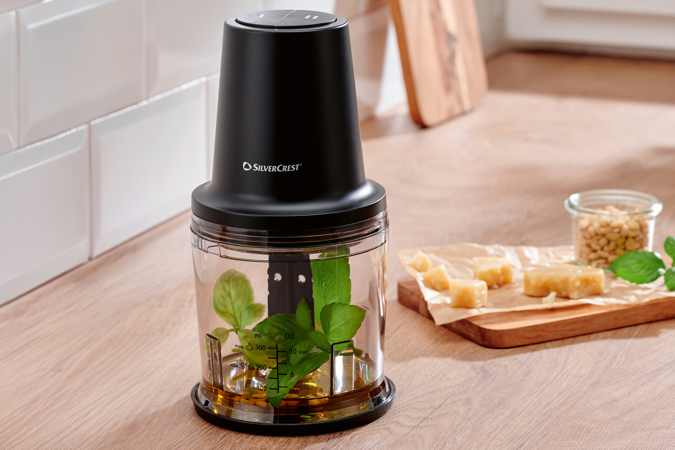 Svart matberedare med basilika, olja och pinjenötter för pesto på en köksbänk.