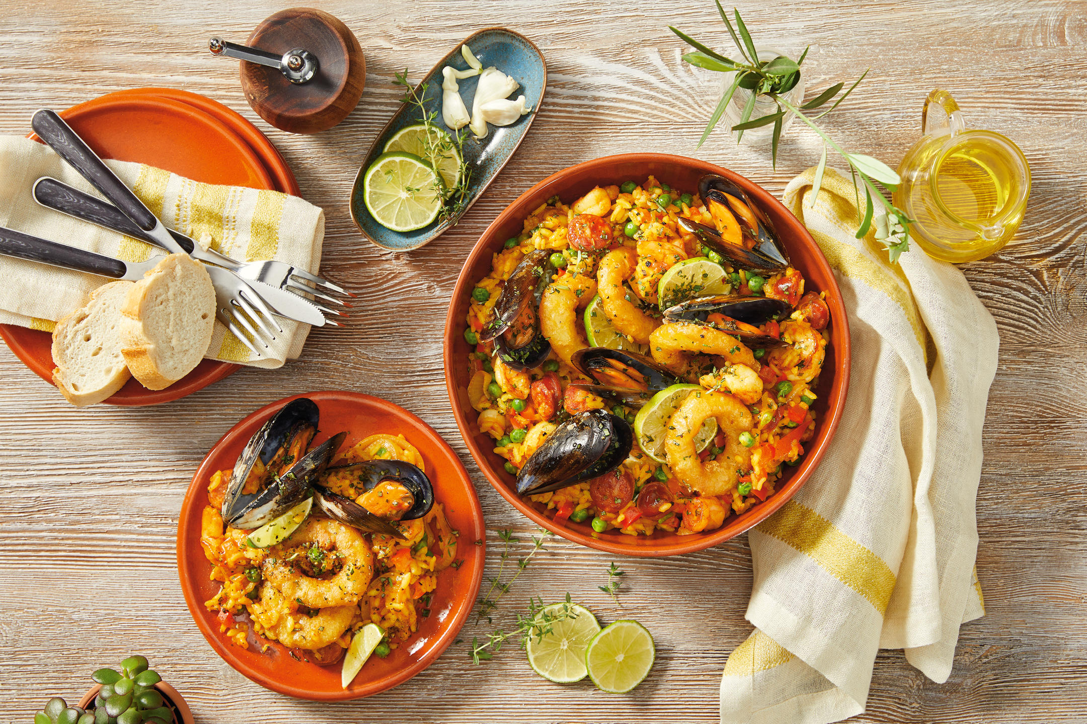 Paella med skaldjur, ris, grönsaker och limeklyftor, serverad med bröd och olivolja.