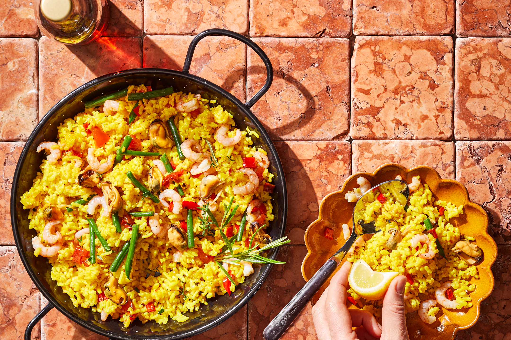Paella med skaldjur, grönsaker och ris i en stor panna, med en portion på en tallrik.